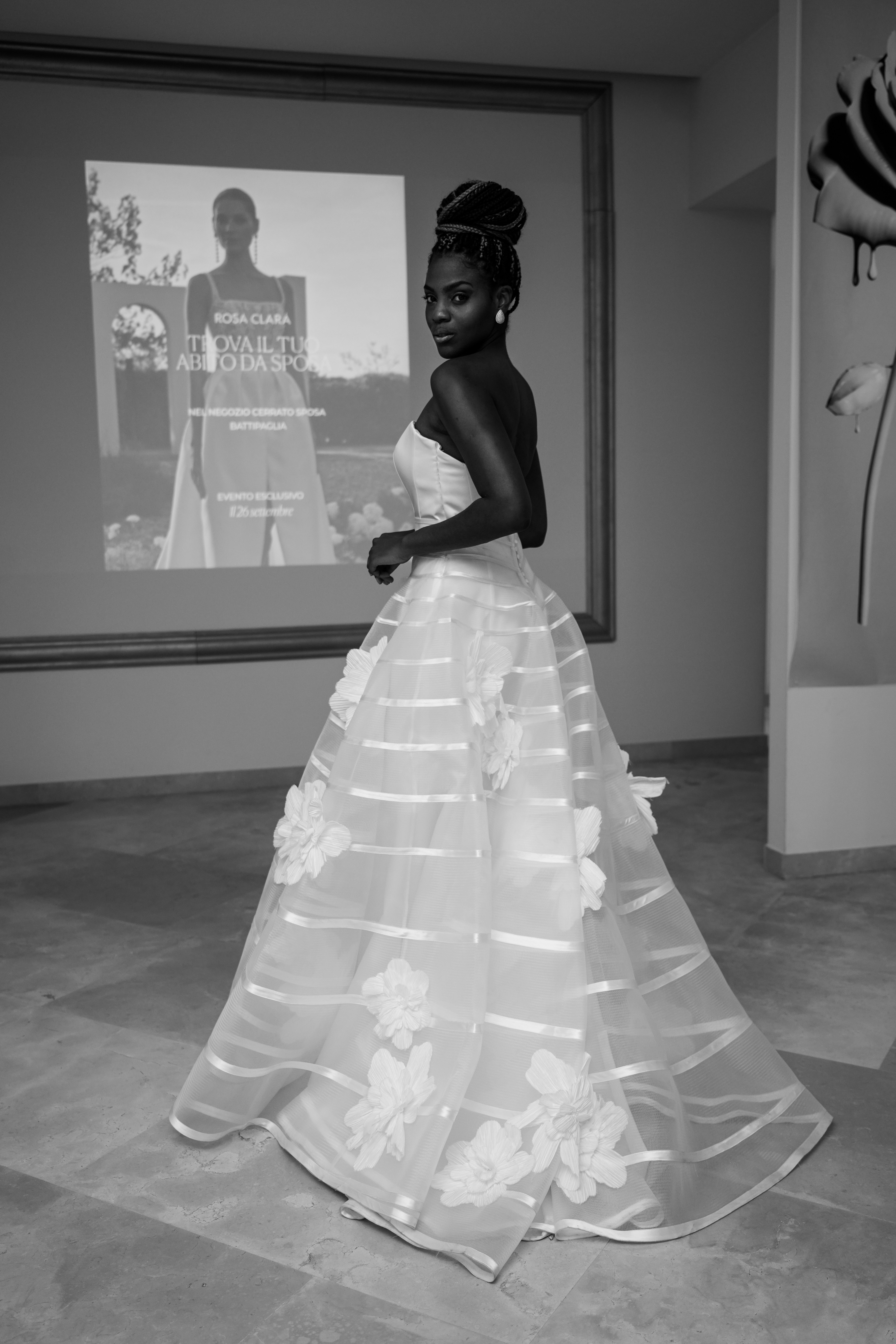 A woman in a strapless white gown with floral appliqués looking over her shoulder