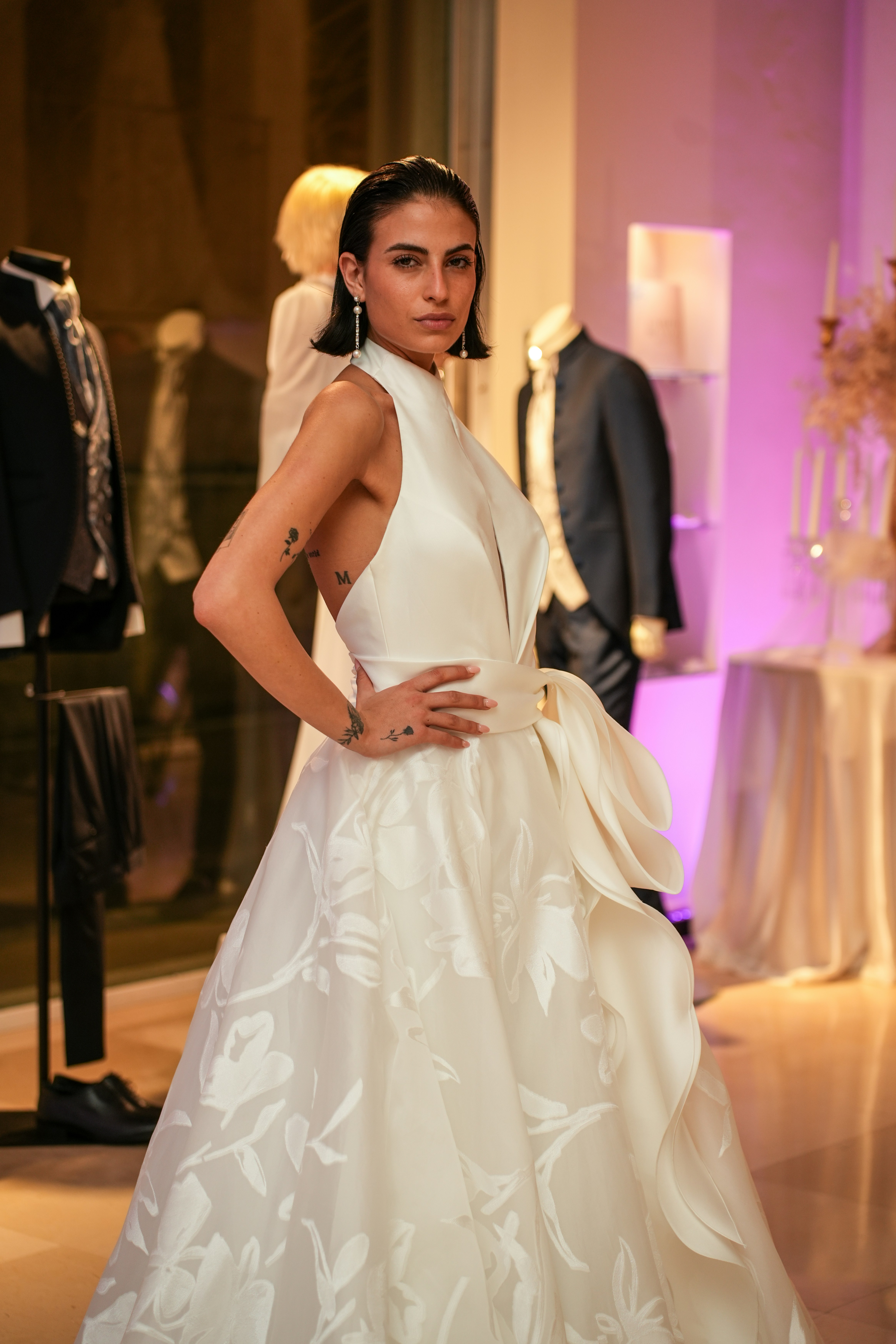 A woman in a white floral wedding dress posing in a formal clothing store