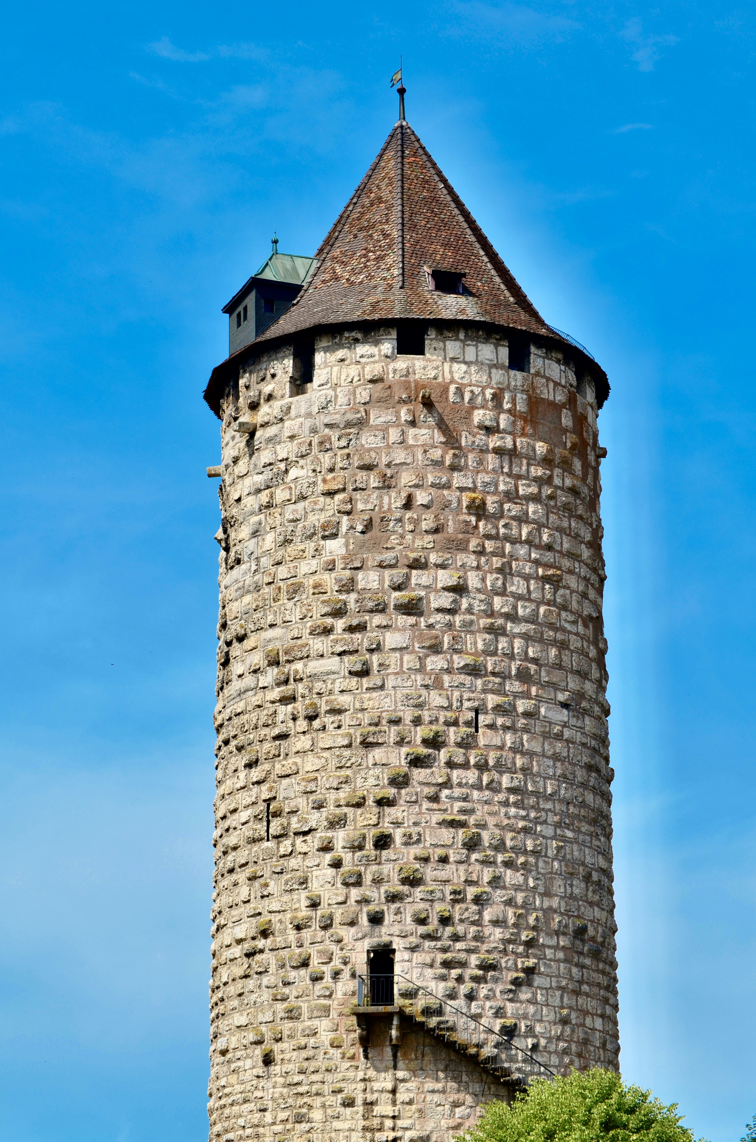 A tall cylindrical stone tower with a conical roof against a clear blue sky