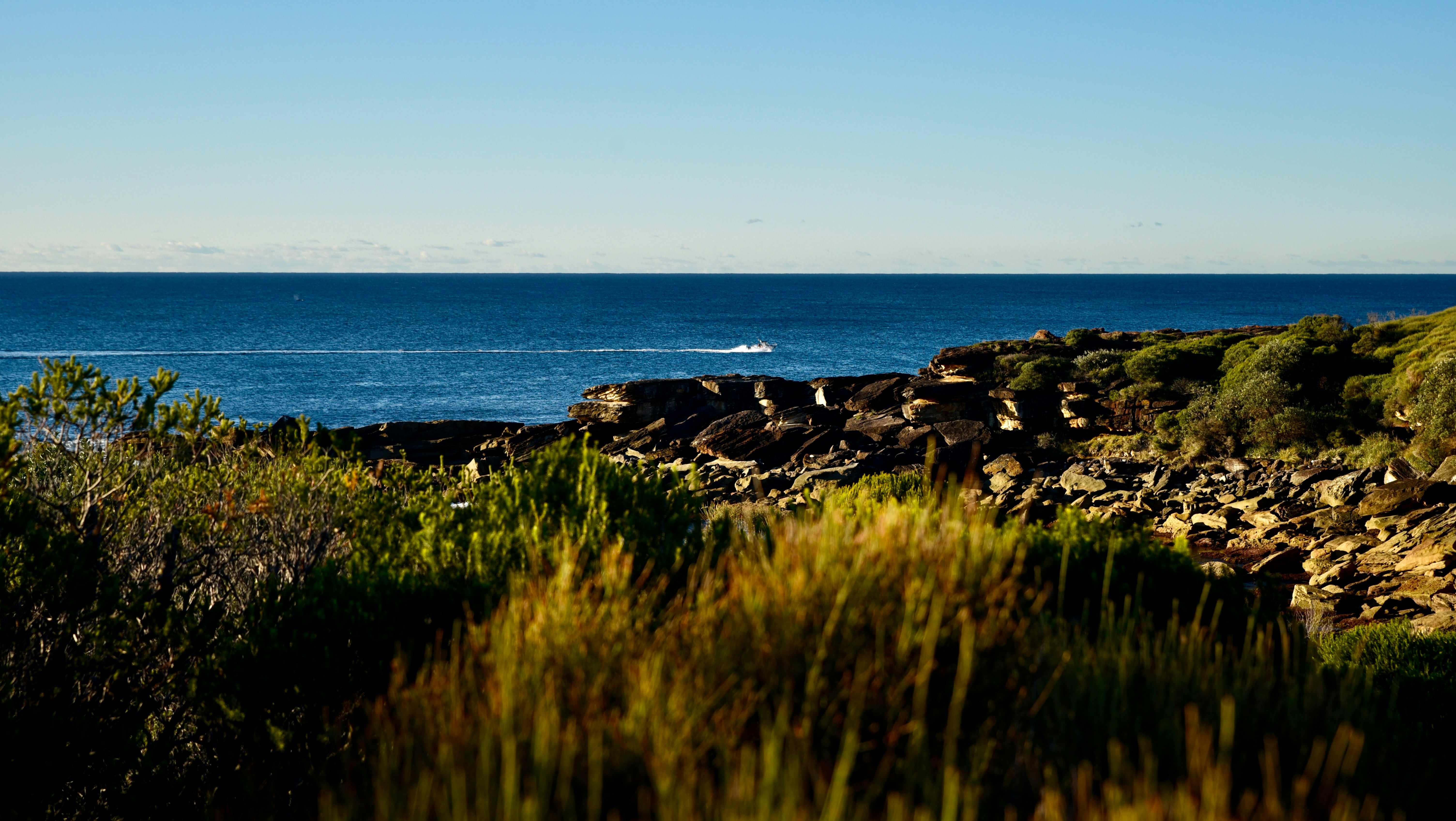 A small boat leaving a wake on the blue ocean near a rocky coastline