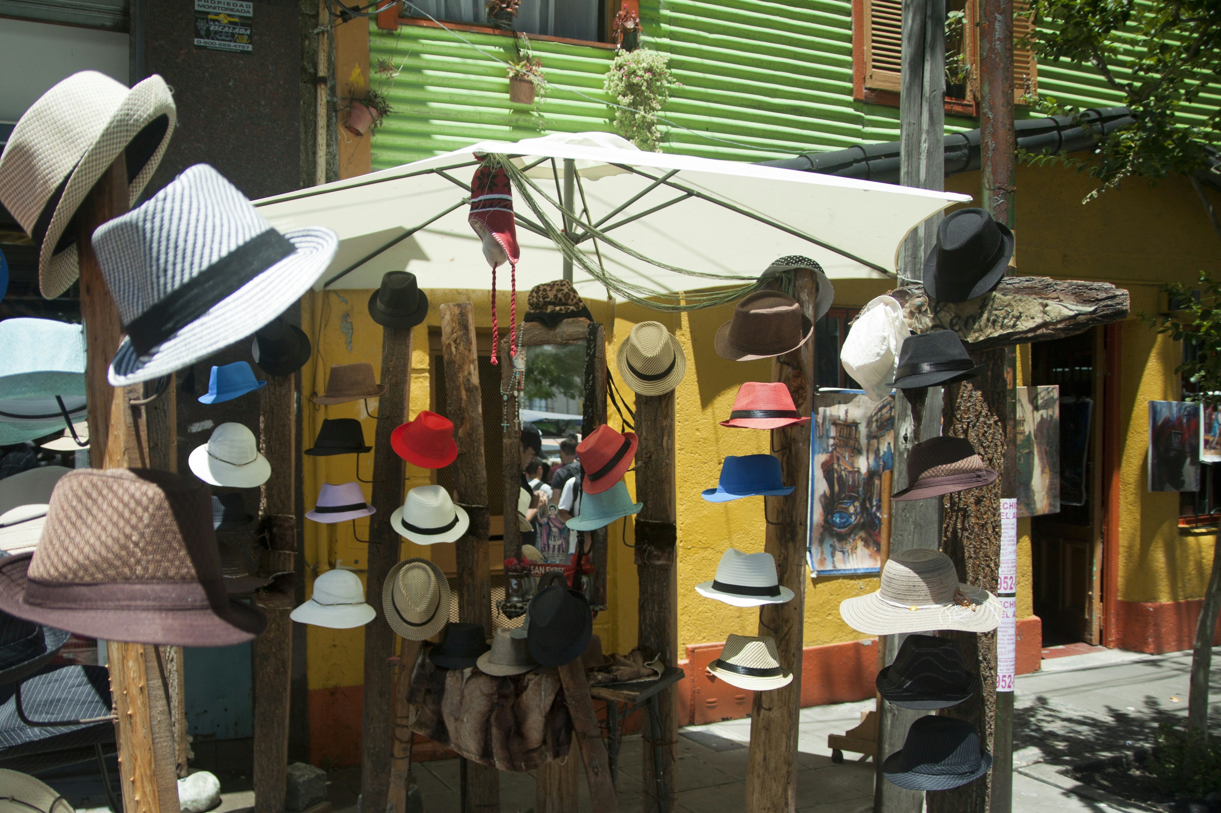 Many colorful fedoras displayed on wooden posts under a white umbrella in La Boca