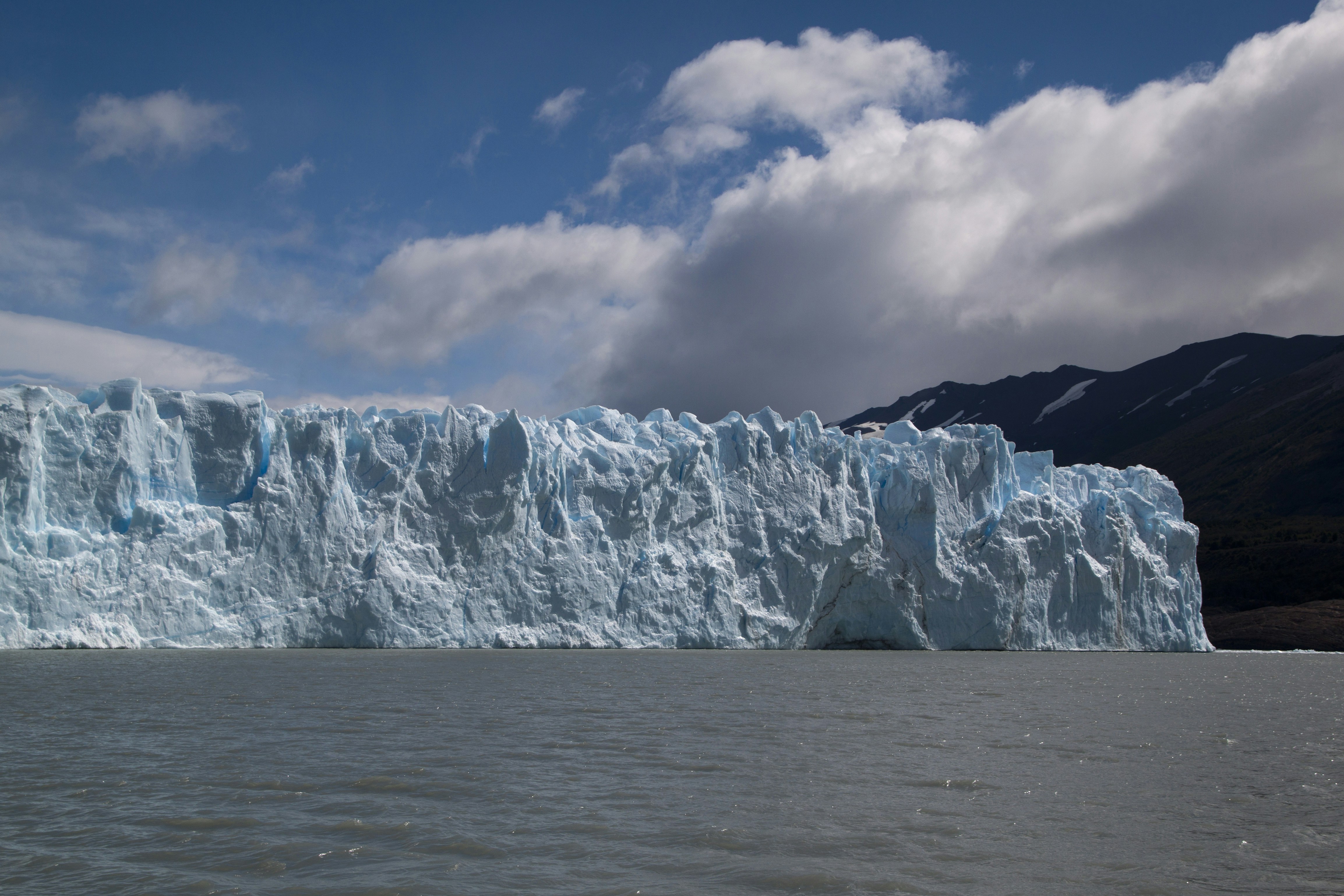 A massive blue glacier wall rising above dark water under a cloudy sky
