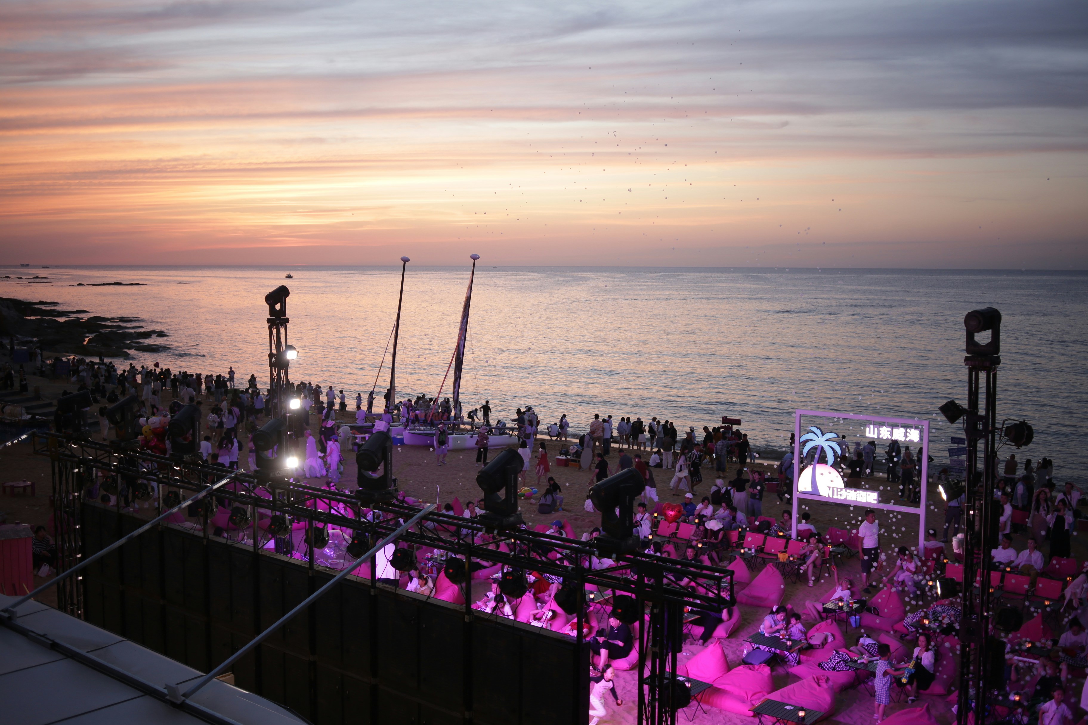 A beach party with pink beanbag chairs and stage lighting at golden hour