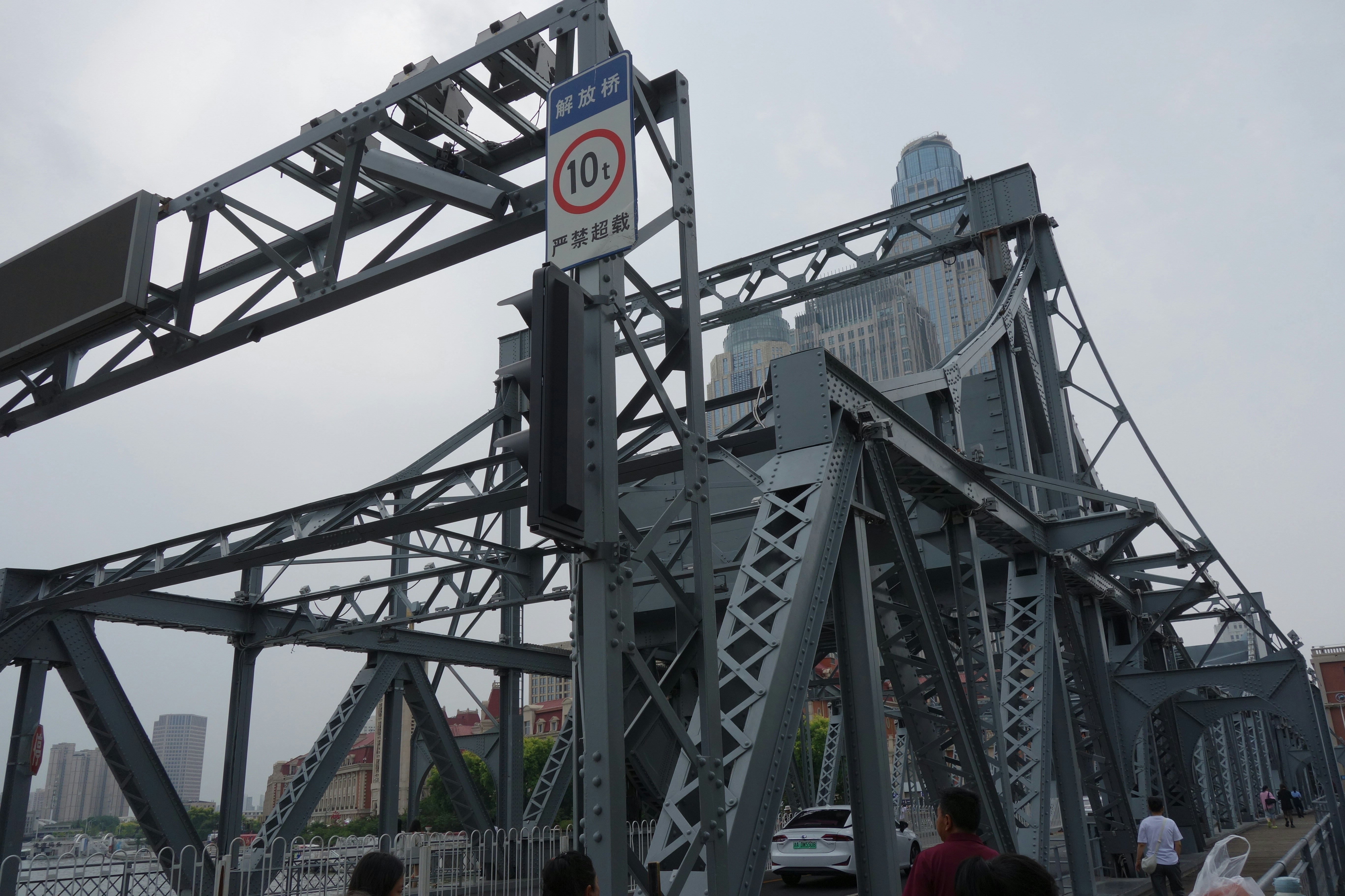 A grey steel truss bridge with a weight limit sign in Tianjin