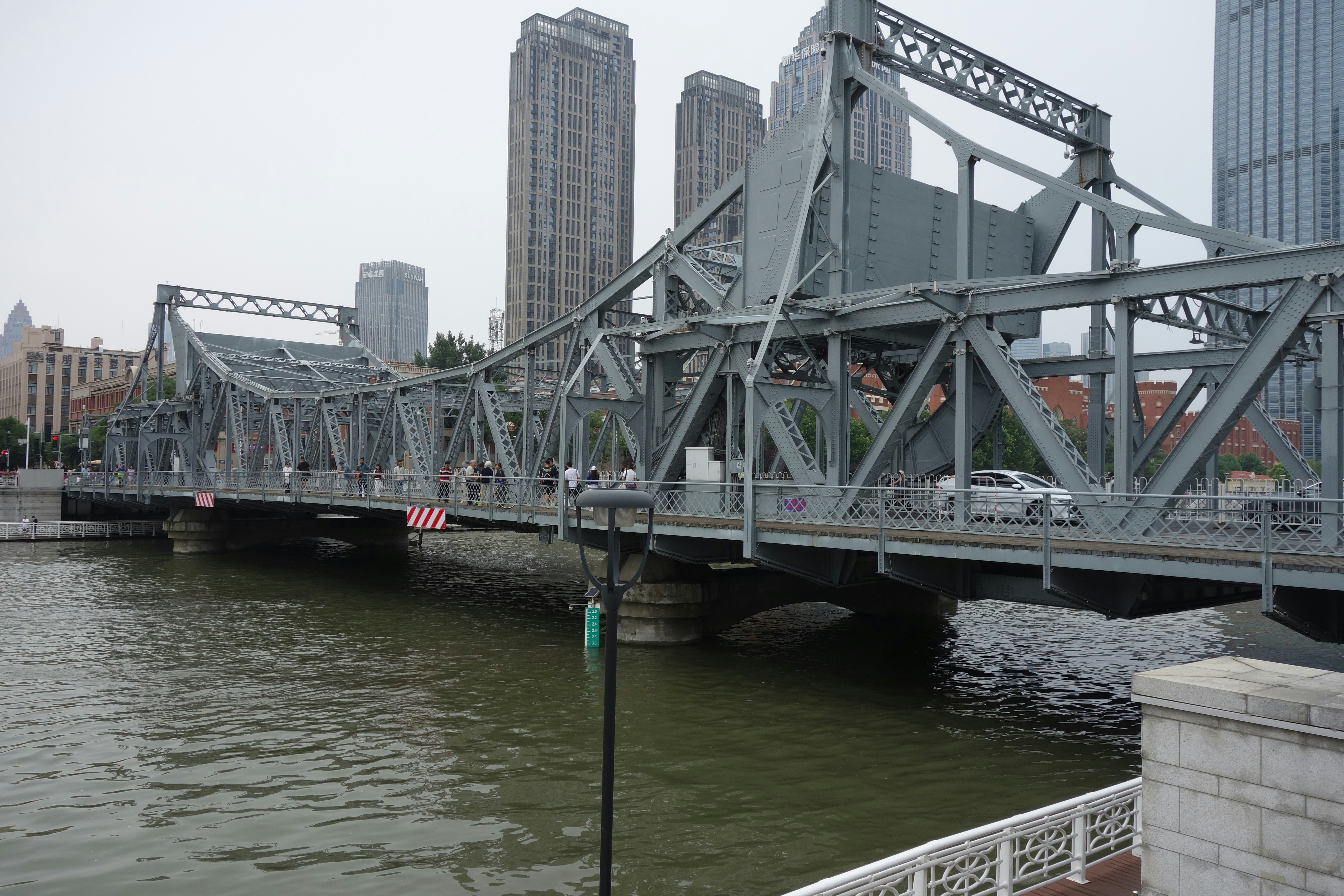 A grey steel truss bridge over a river with pedestrians and a car