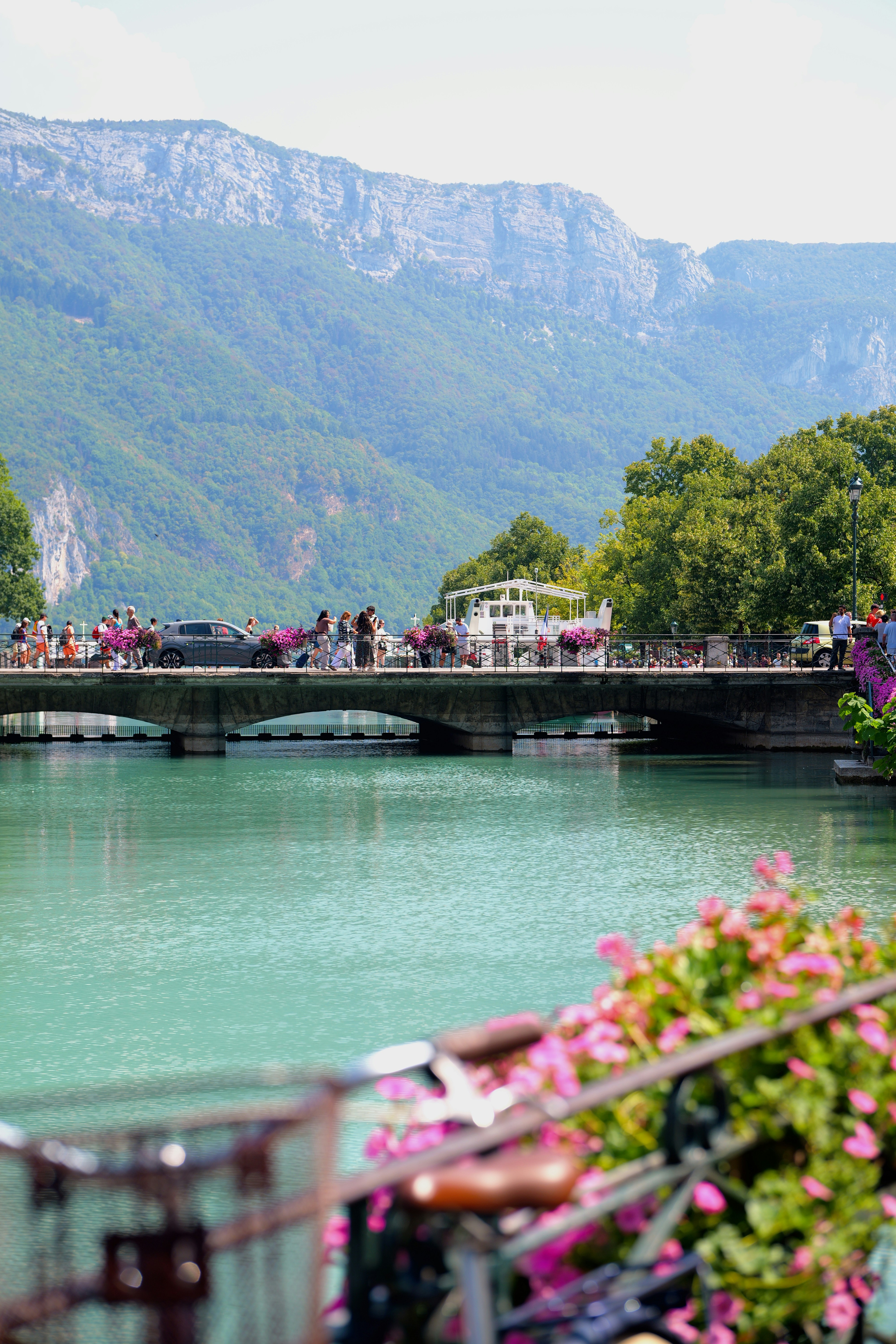 People walking across a stone bridge over a turquoise canal with mountain scenery