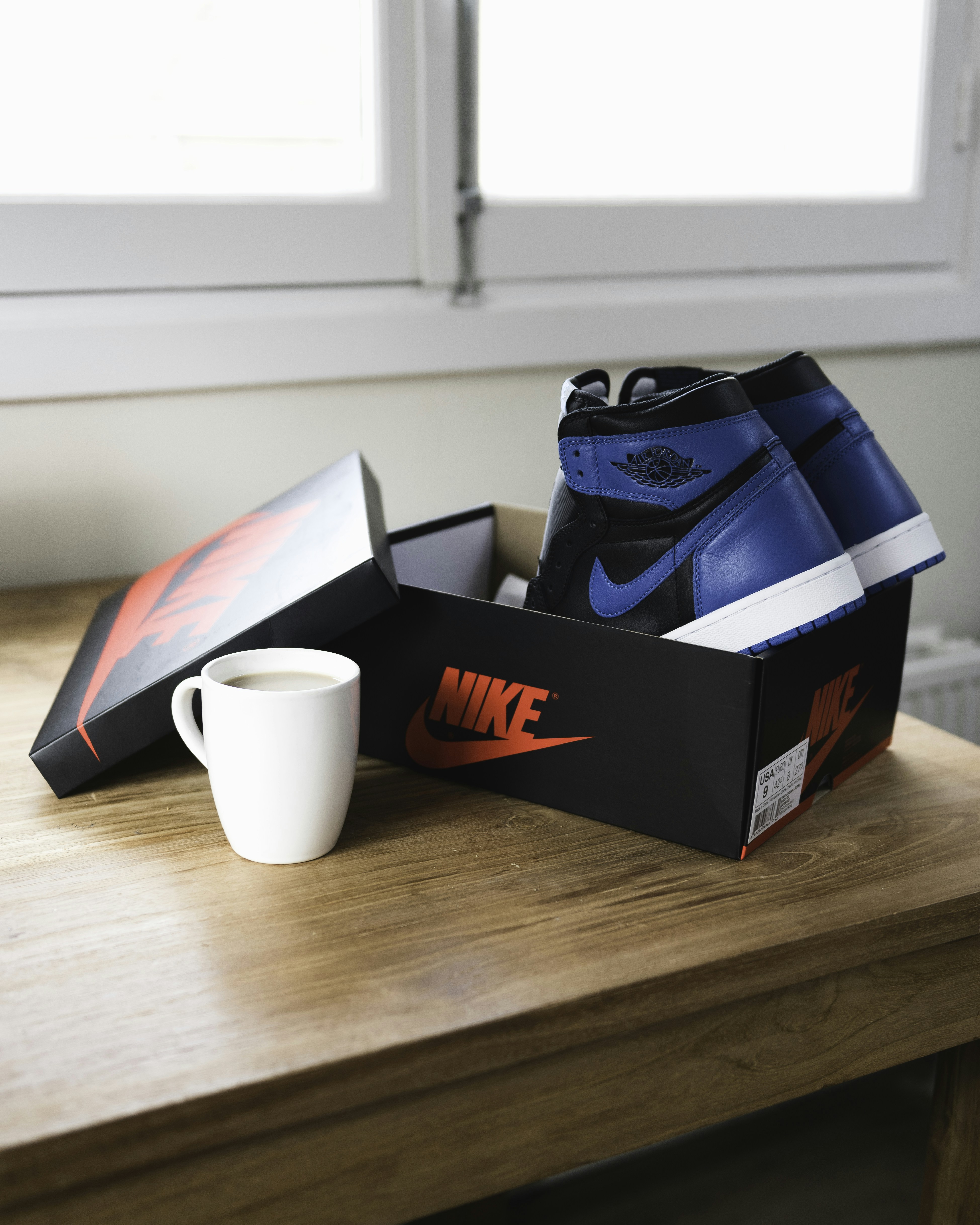 Blue and black high-top sneakers in a shoebox beside a white coffee mug