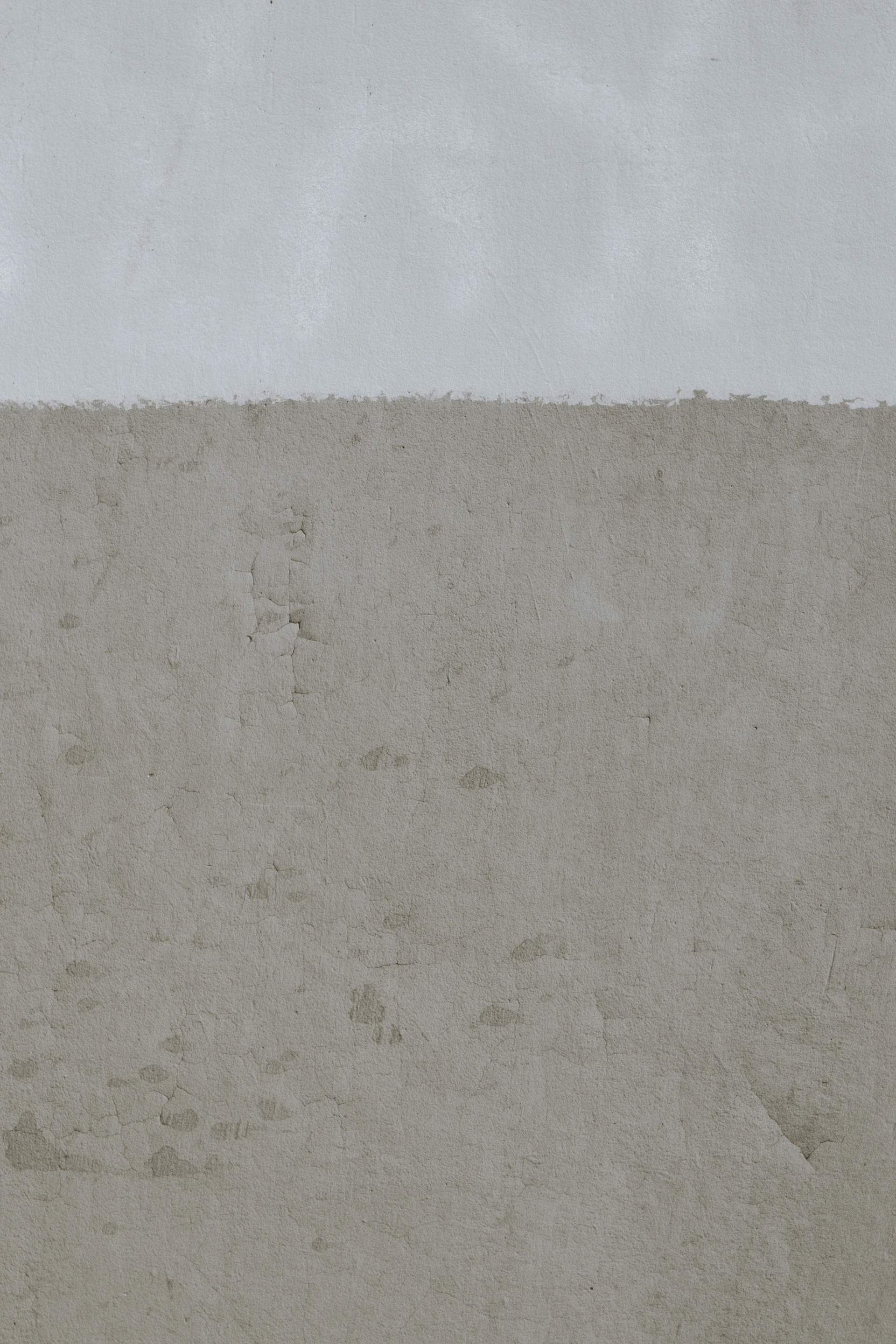 A wall with a smooth light grey upper section and a textured beige lower section