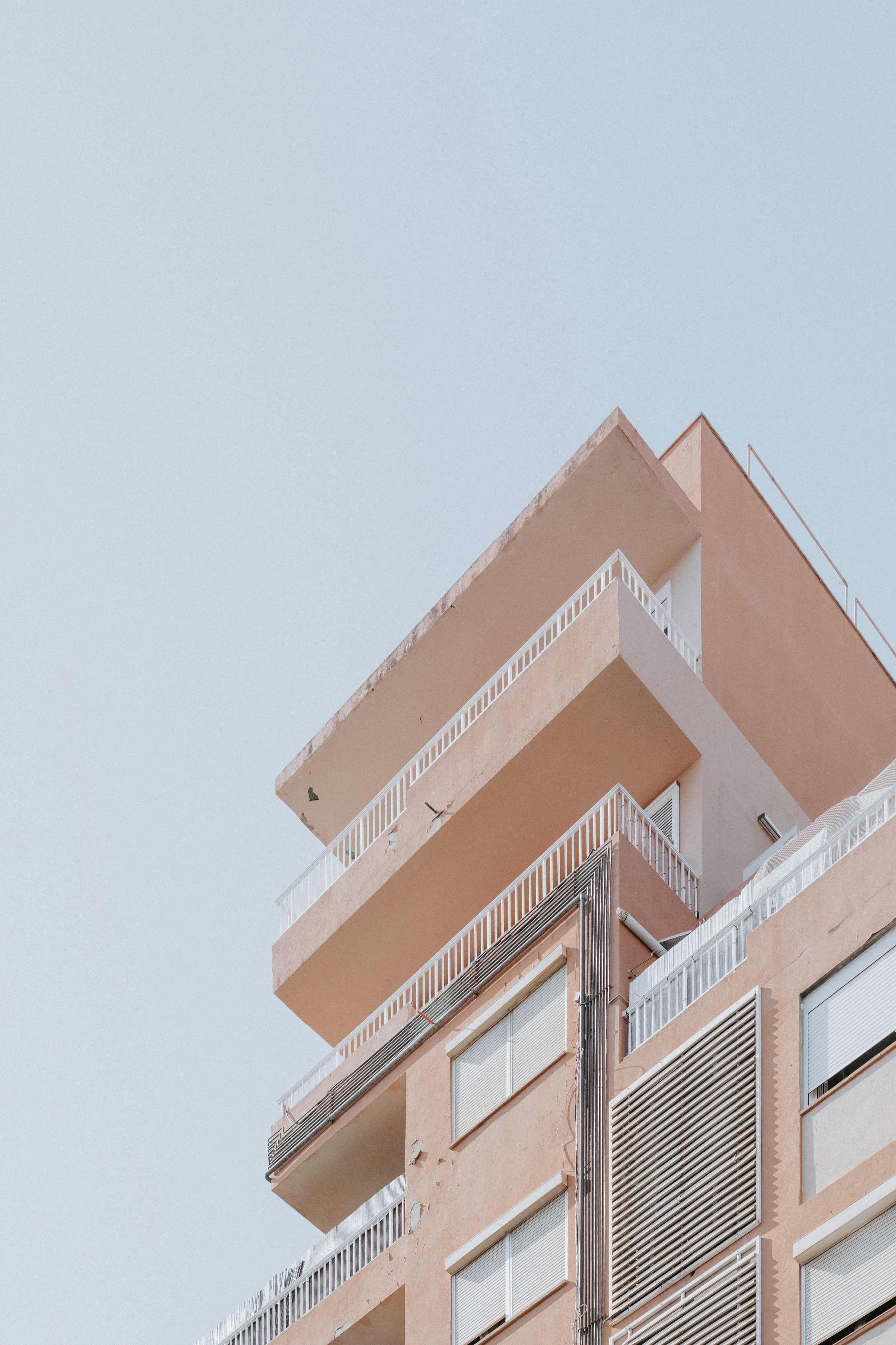 A peach colored apartment building with balconies against a clear pale sky