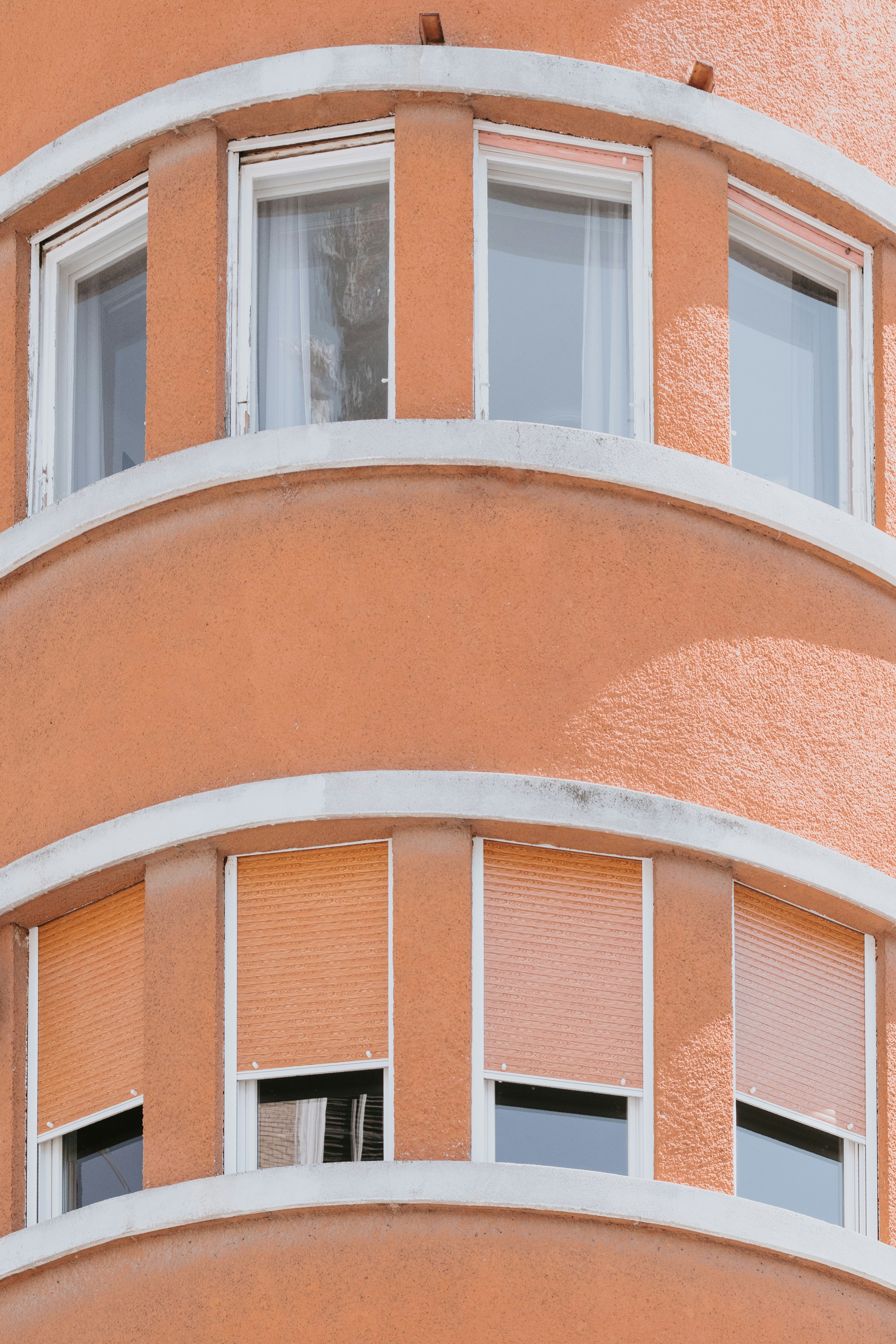 Curved orange building facade with white window frames and closed roller shutters