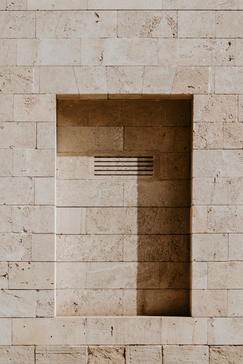 A recessed rectangular niche in a beige stone wall with a horizontal vent
