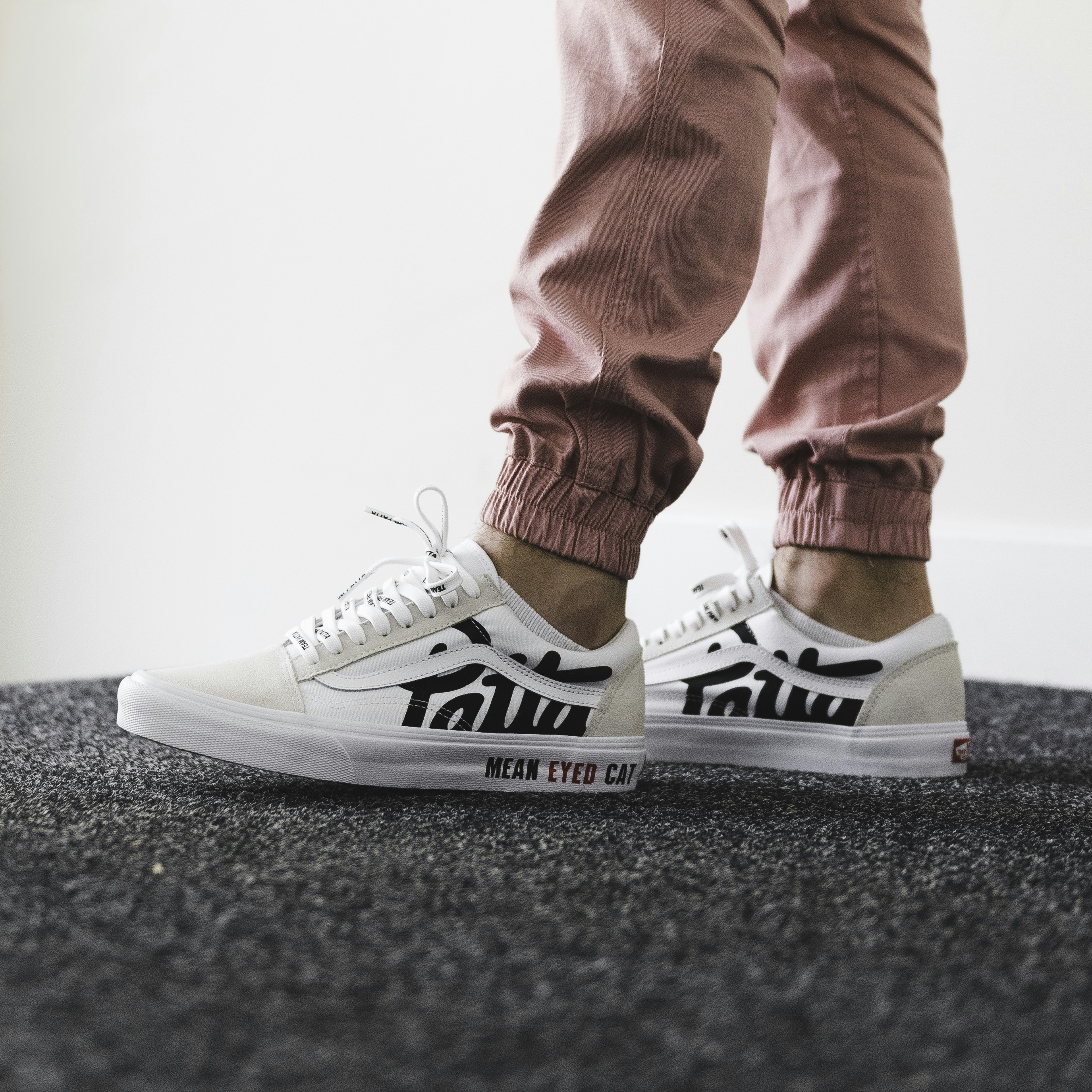 A person wearing pink joggers and white sneakers with black lettering on a grey carpet