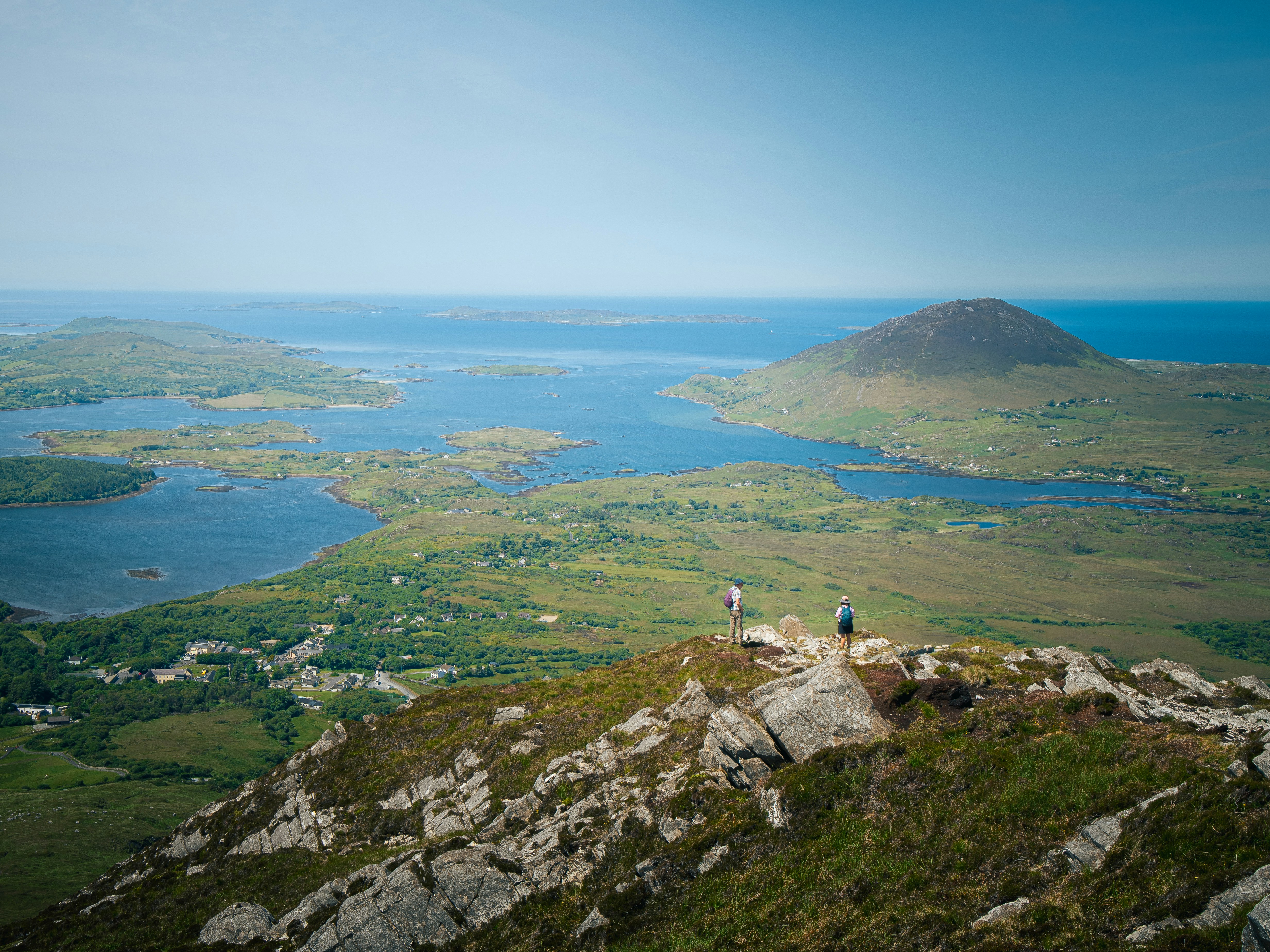 Two hikers on a rocky mountain summit overlooking a coastal landscape with islands