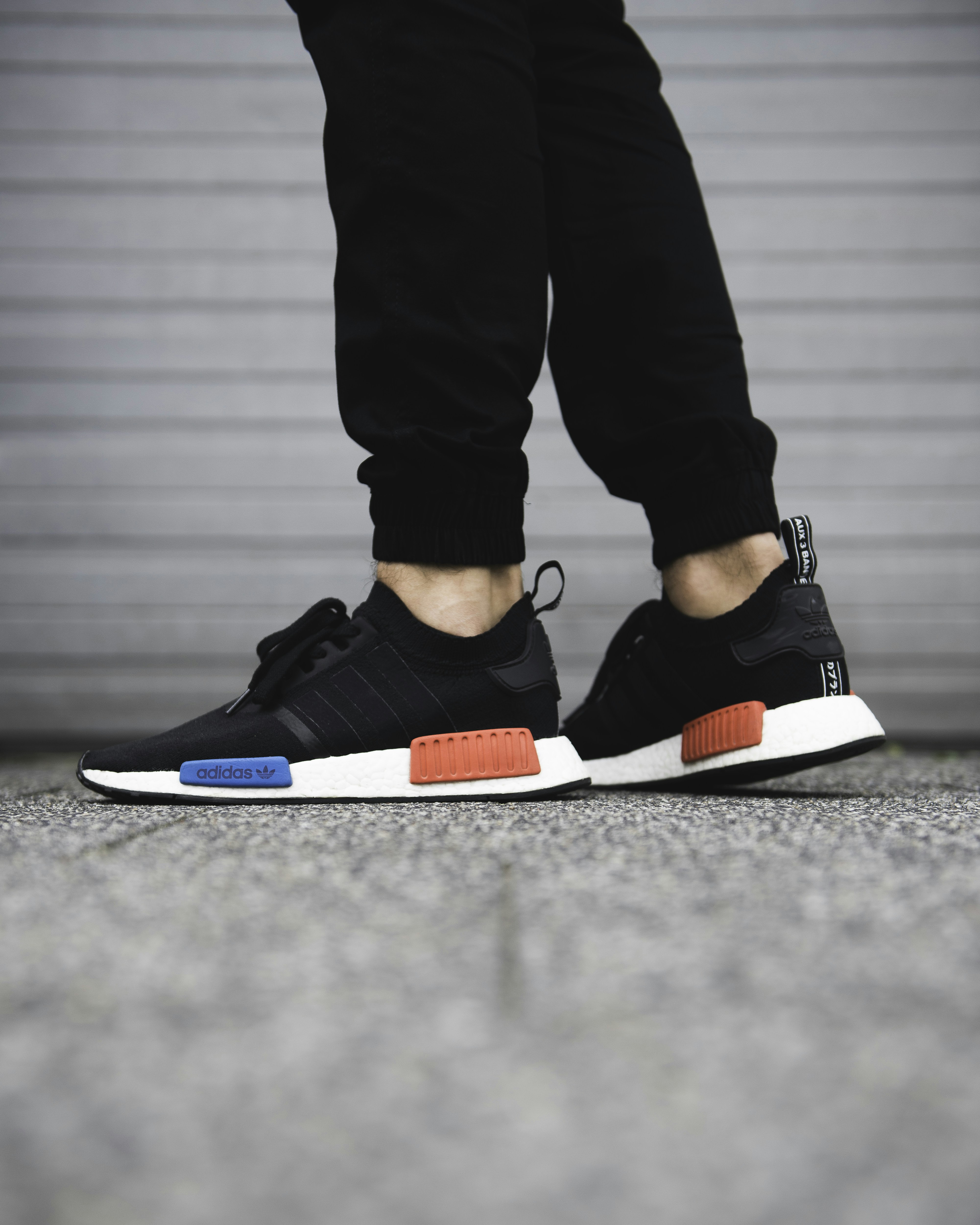 A person wearing black sneakers with white soles and red and blue accents