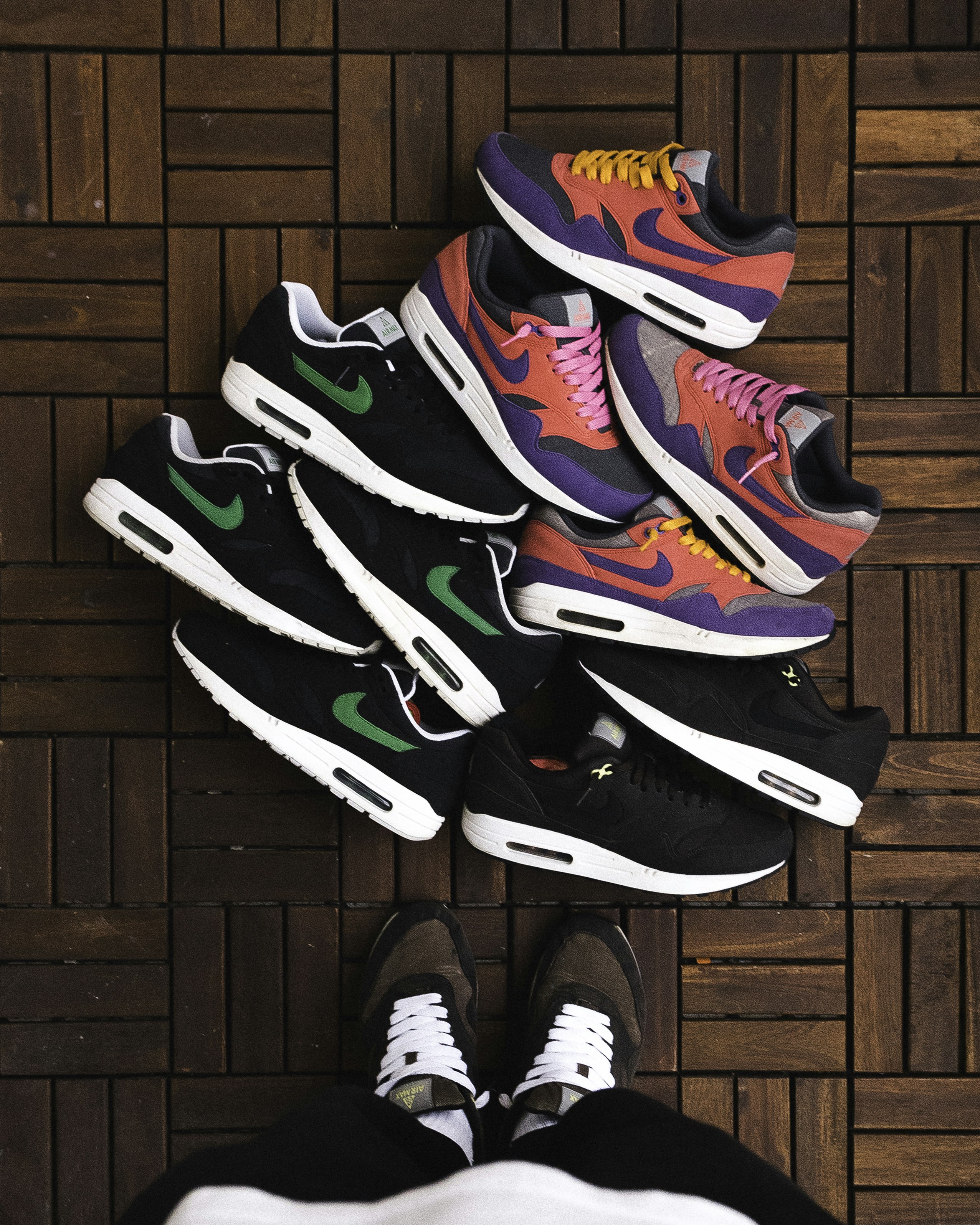 A person wearing brown sneakers standing over a pile of colorful athletic shoes
