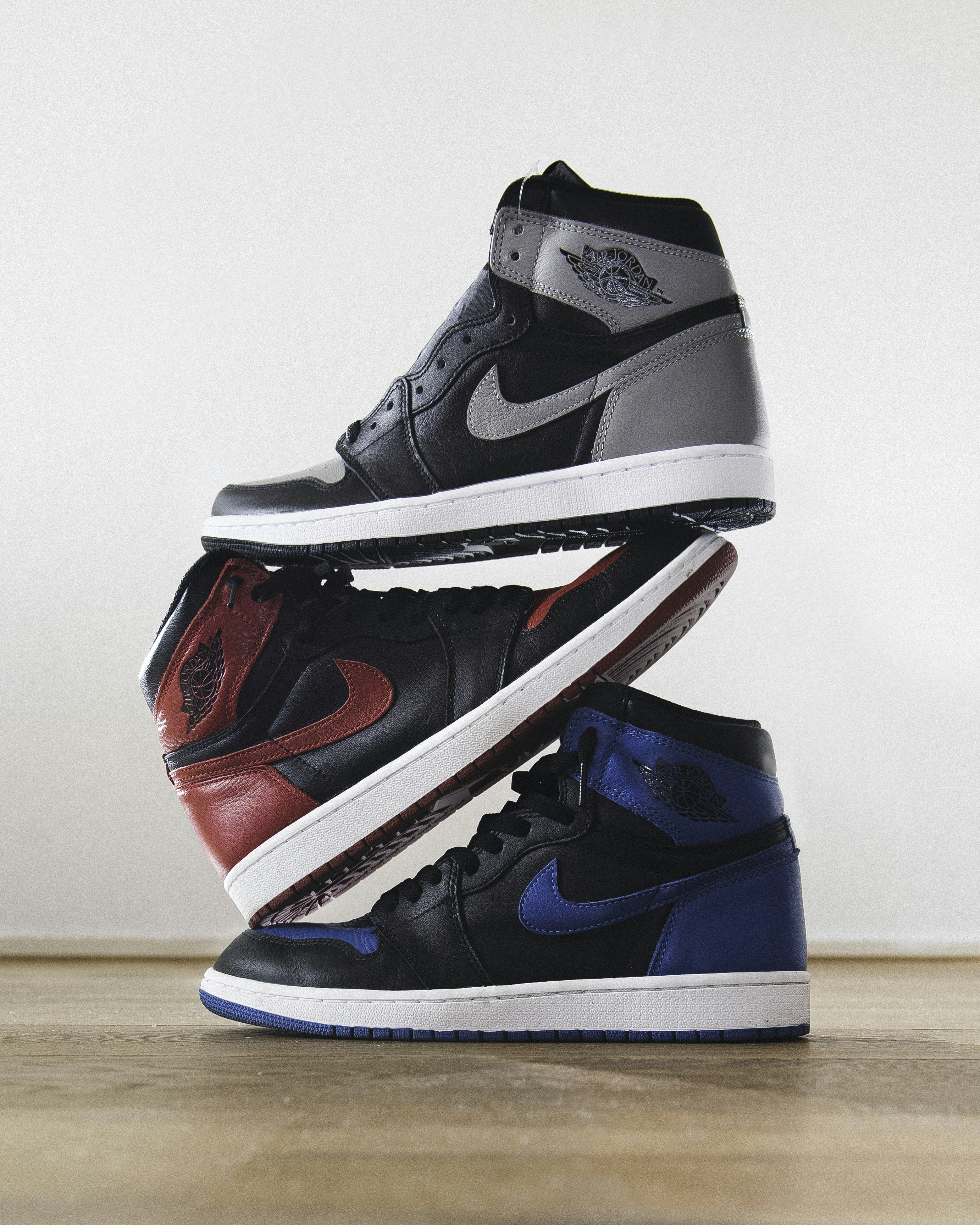 Three high-top sneakers in grey, red, and blue stacked on a wooden floor