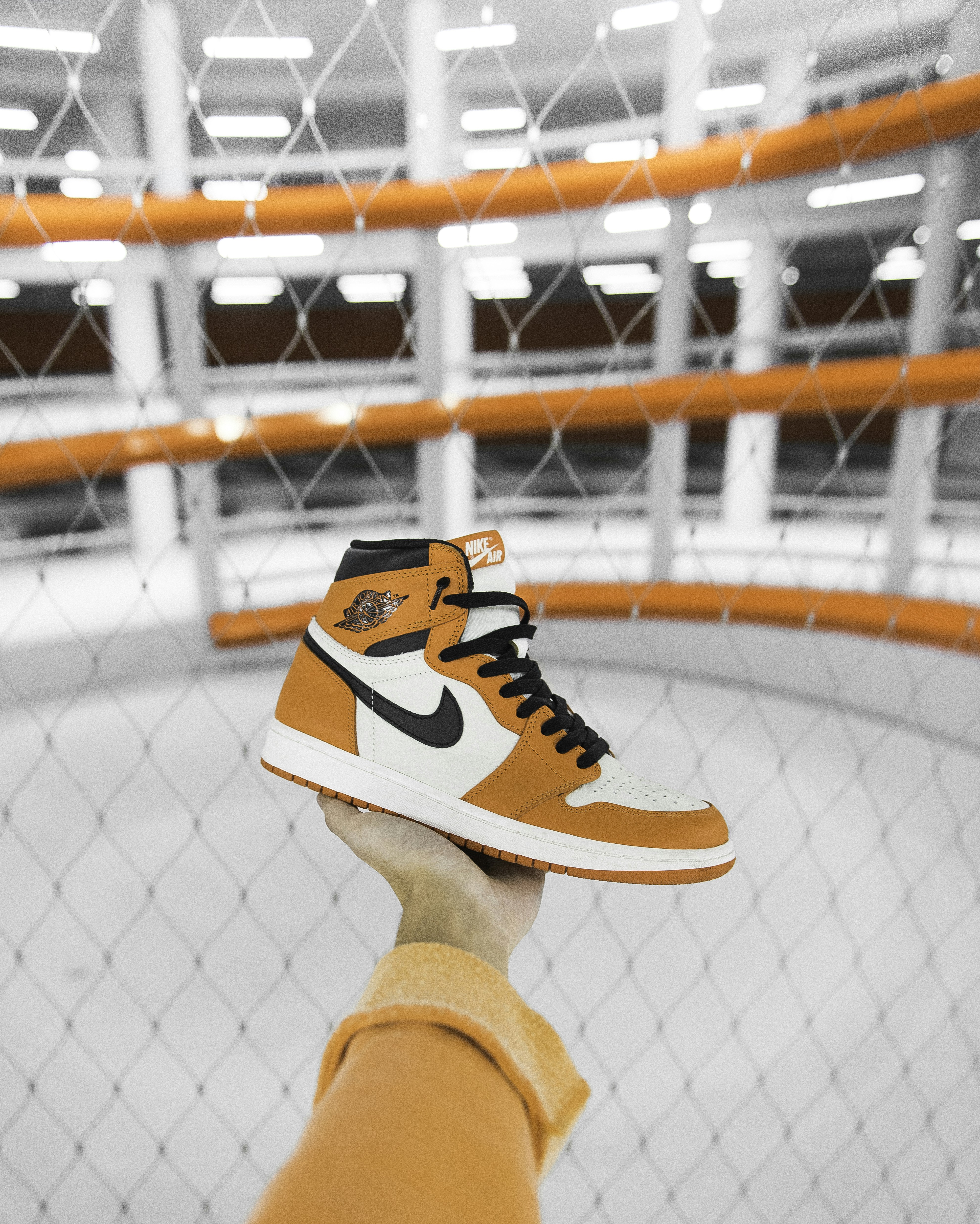 A hand holding an orange and white high-top sneaker against a safety net