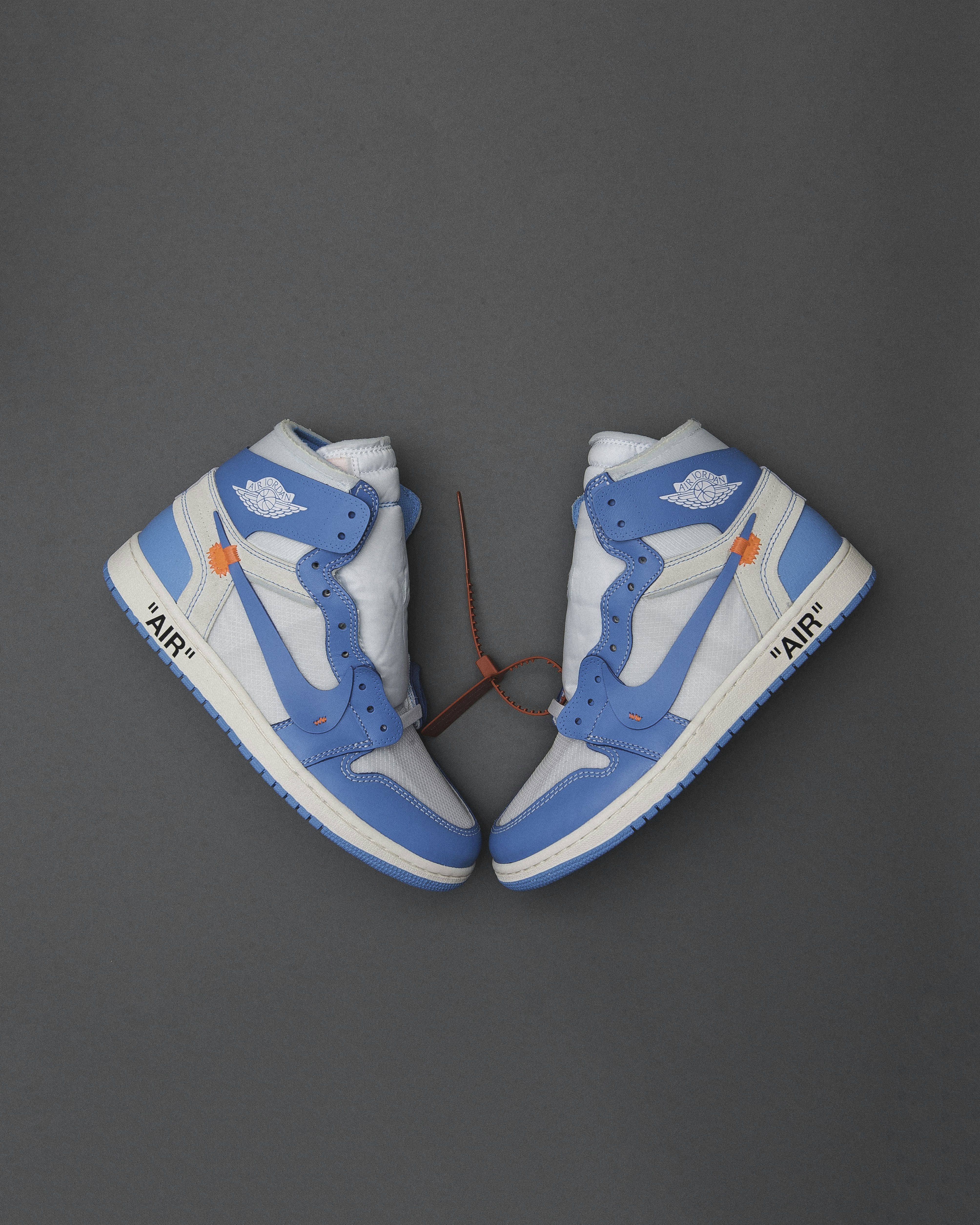 Two blue and white high-top sneakers with a red zip tie on grey