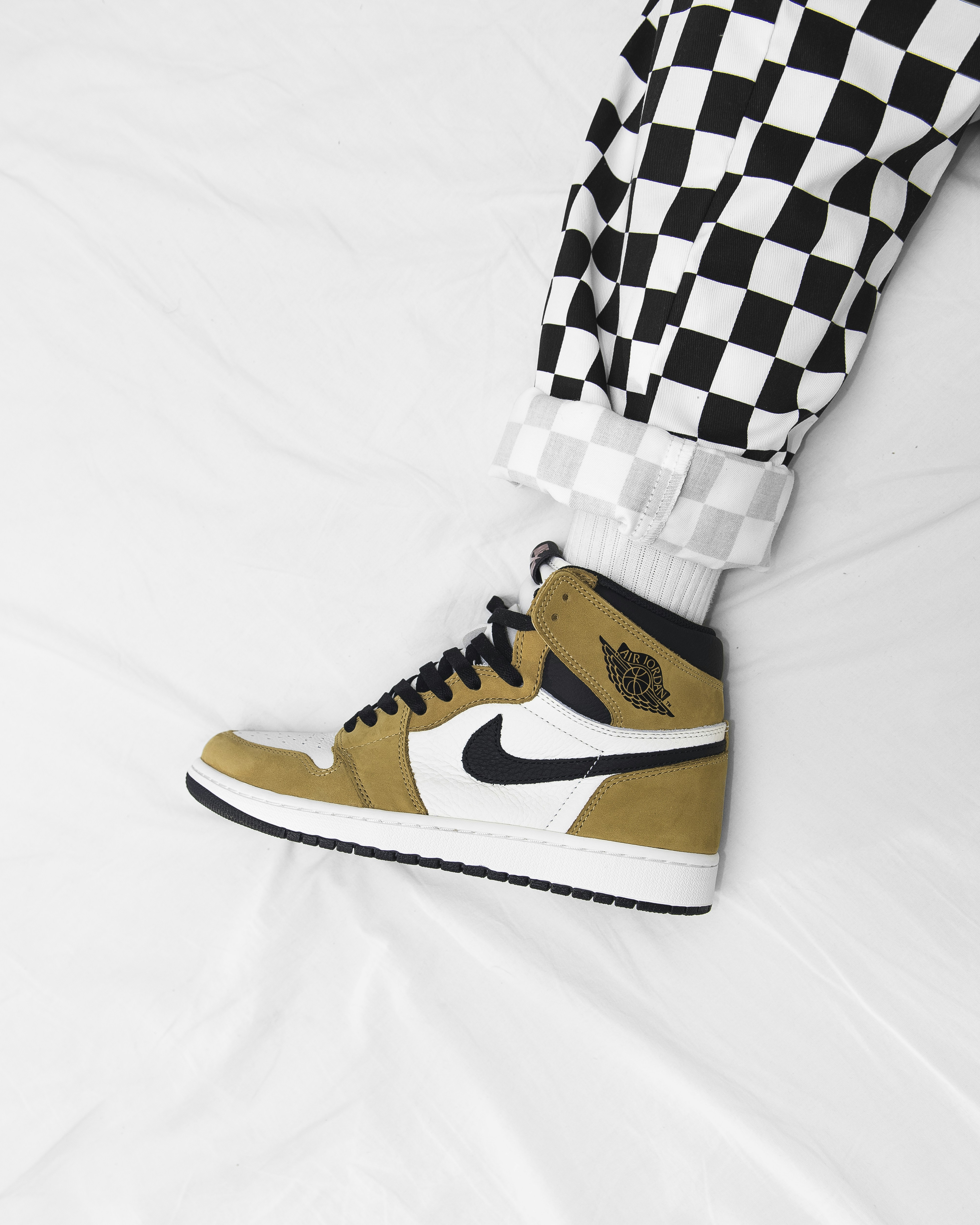 A high-top sneaker in tan, white, and black worn with checkered trousers