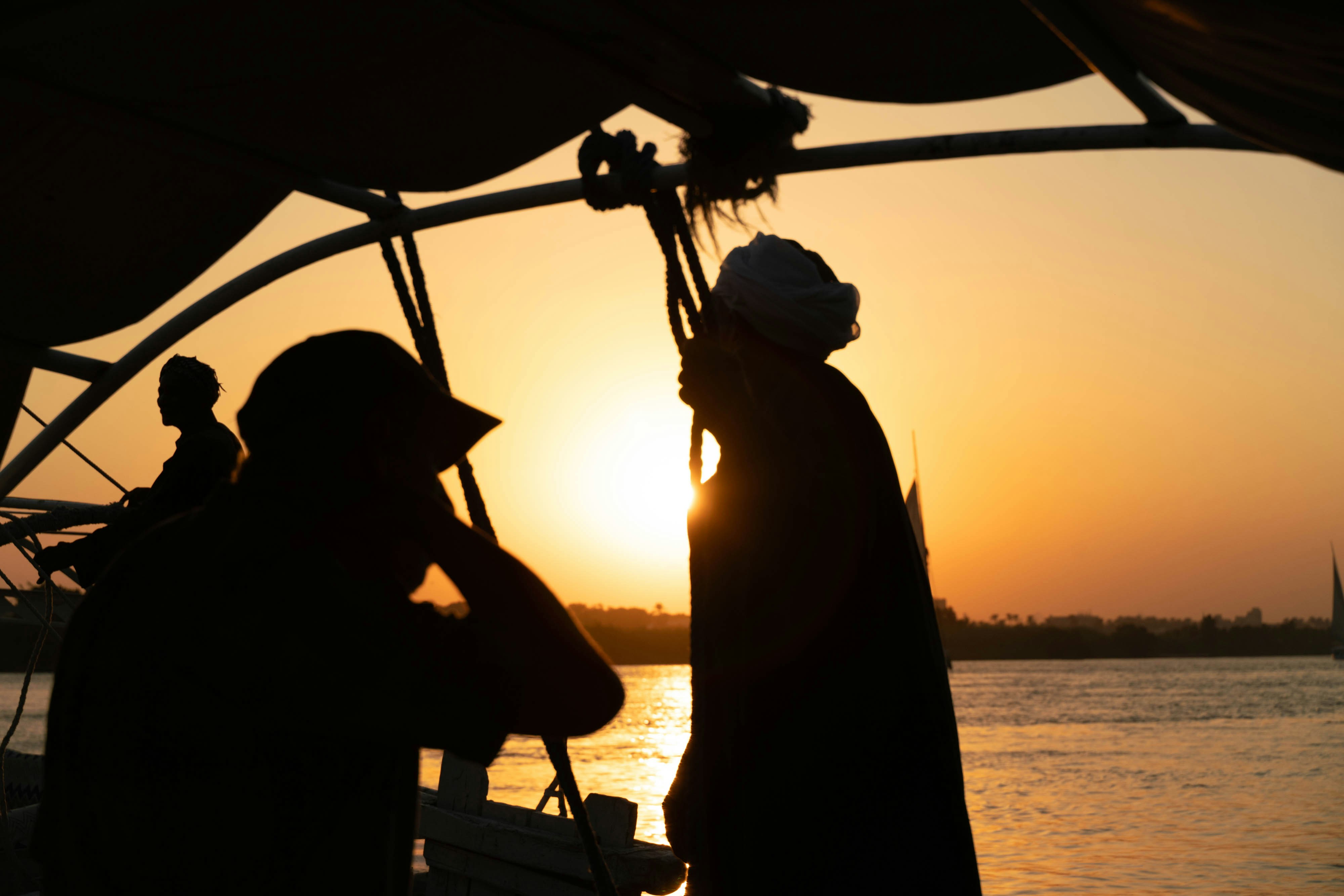 Silhouettes of people on a boat against a warm orange sky at low sun