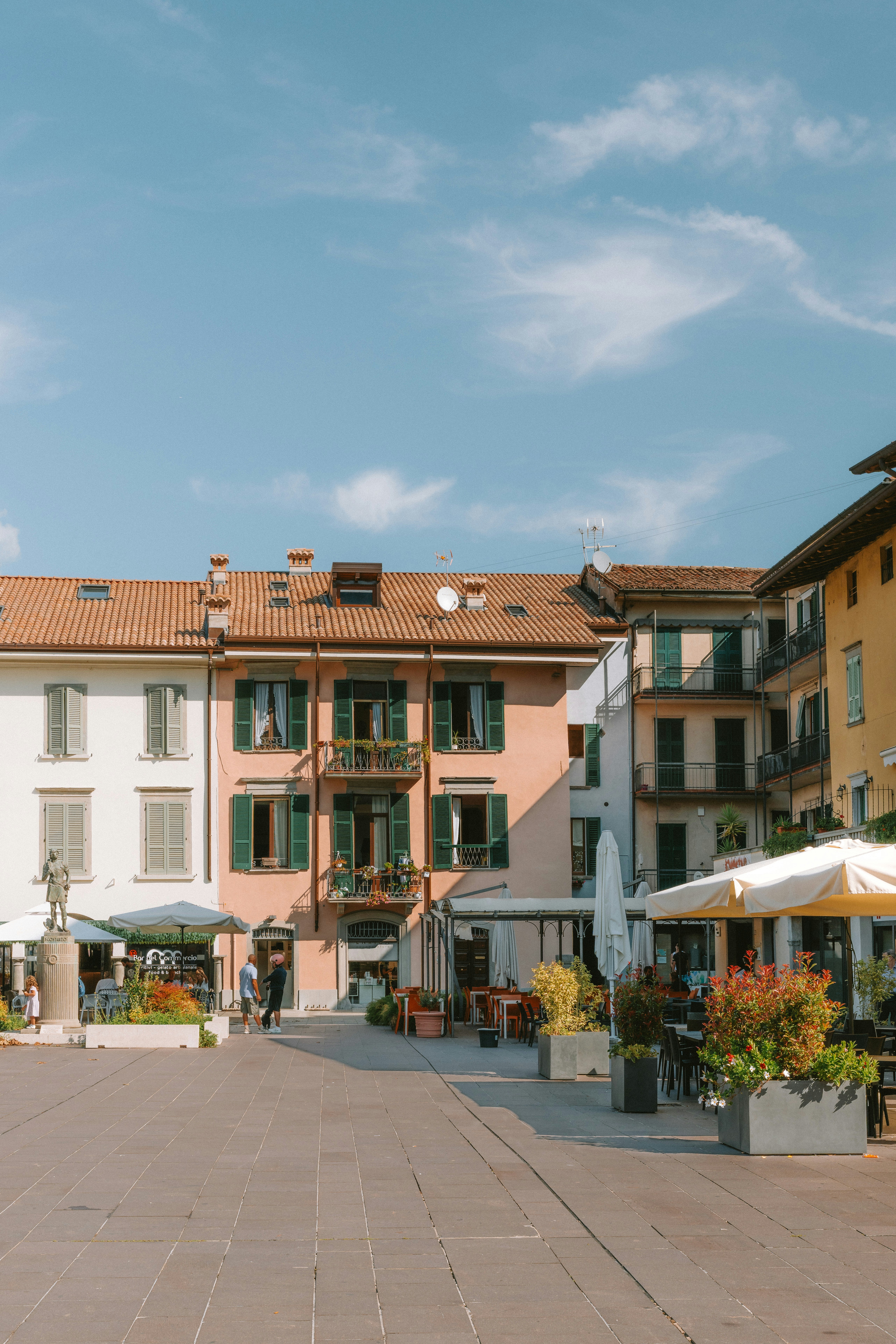 A paved town square with cafe tables and colorful buildings under a blue sky