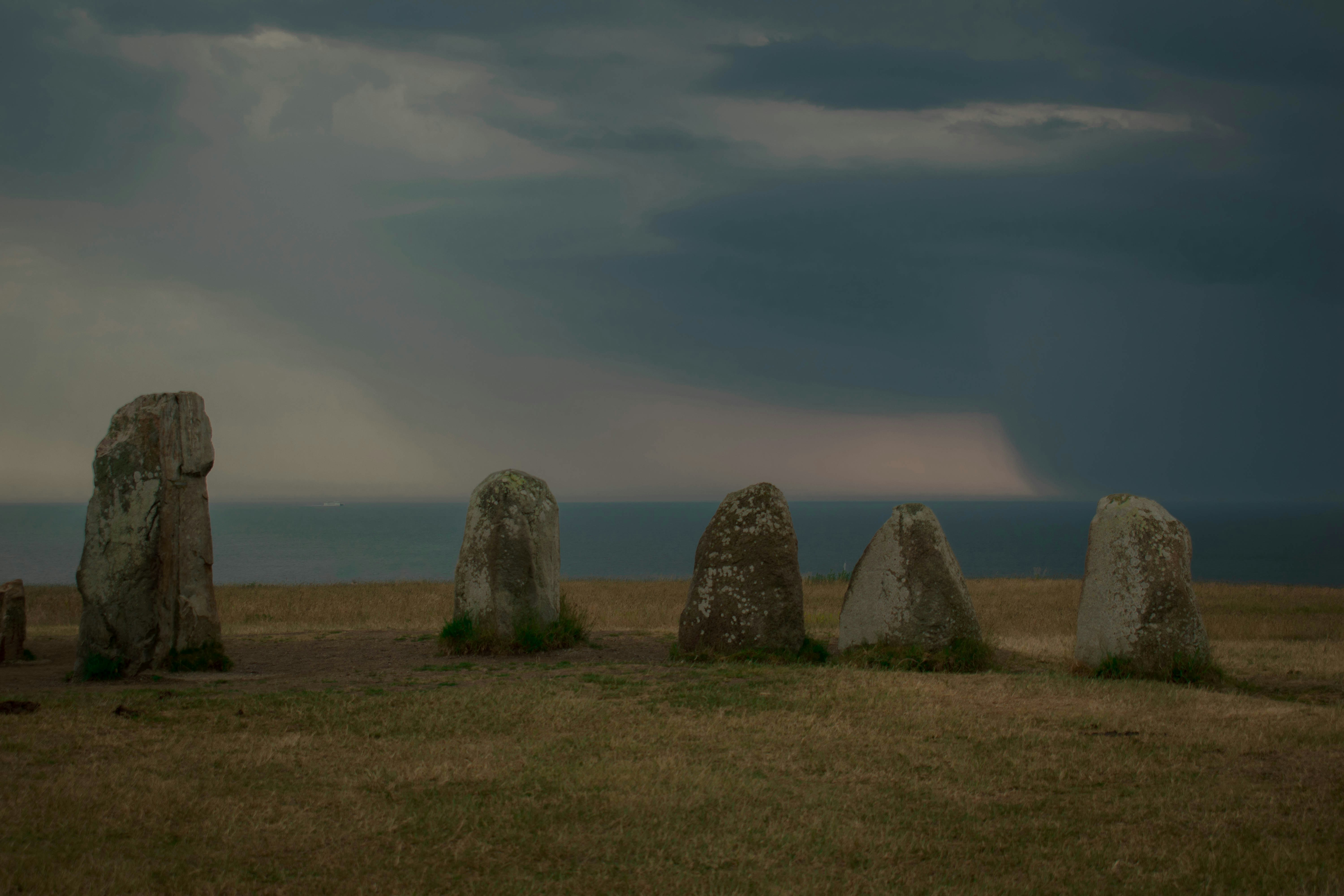 Ancient standing stones in a grassy field overlooking the sea under dark storm clouds