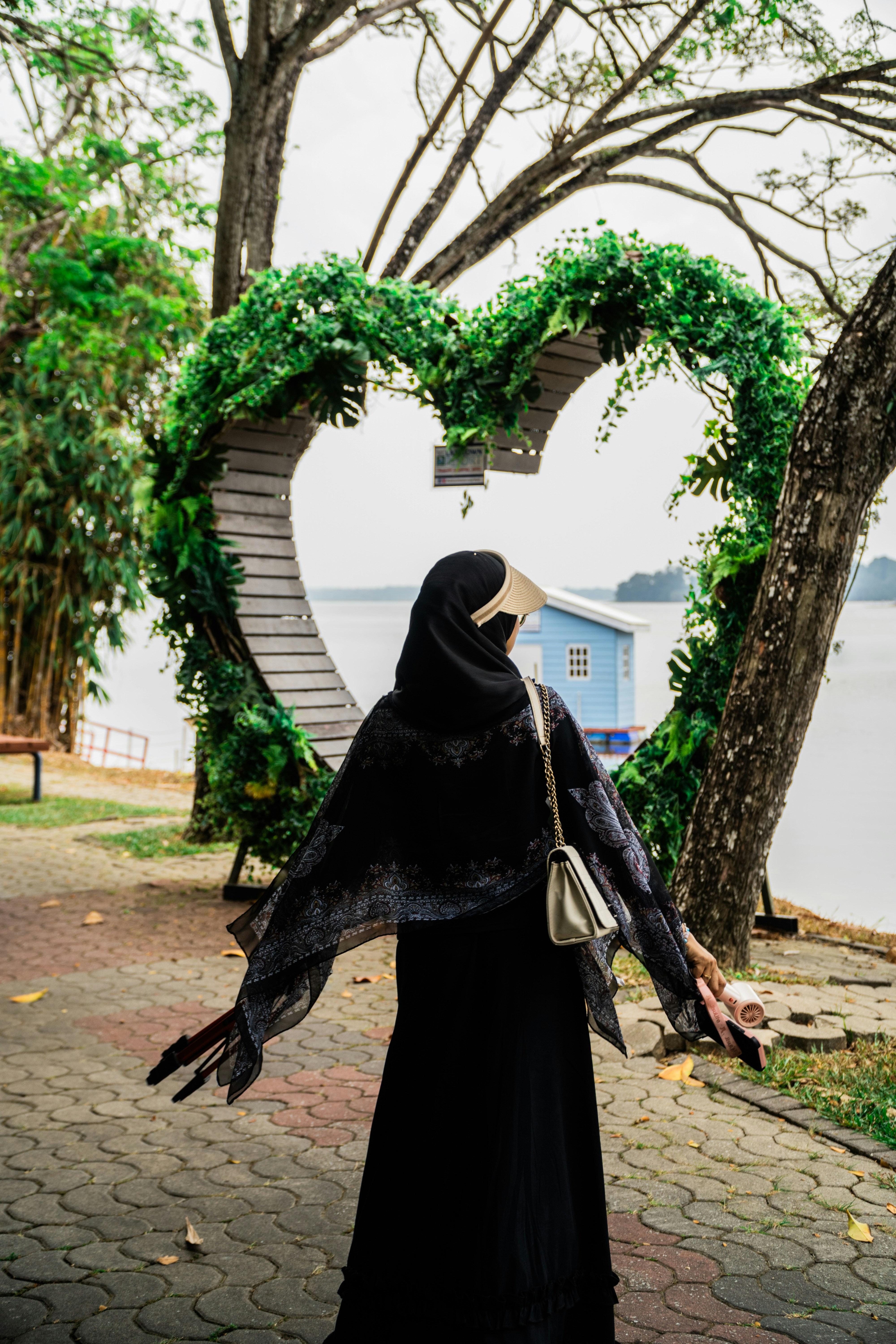 A person in a black hijab and shawl standing before a heart-shaped archway