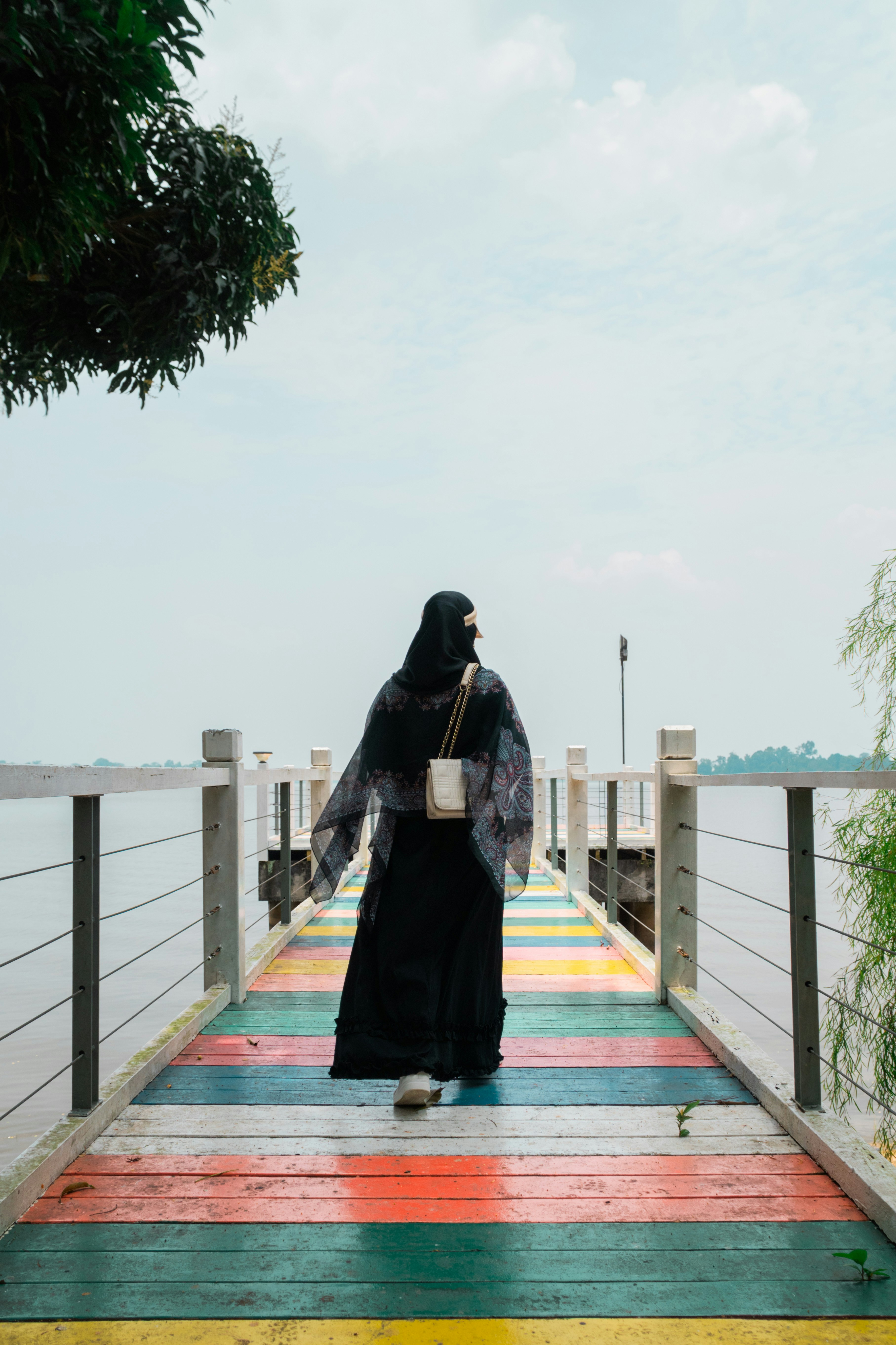 A person in a black abaya walking on a colorful wooden pier over water