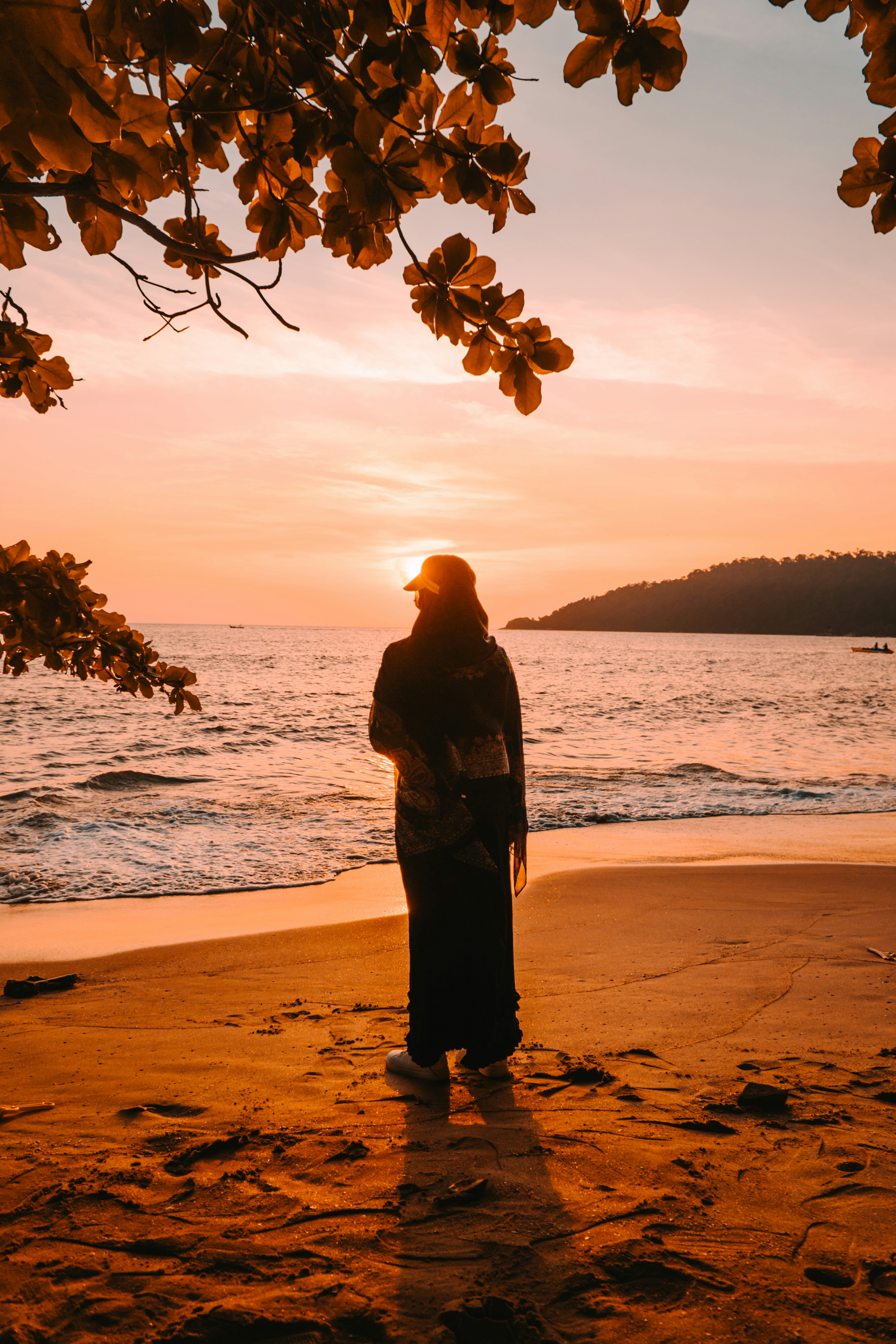 A person in a long skirt and head covering on a beach at golden hour