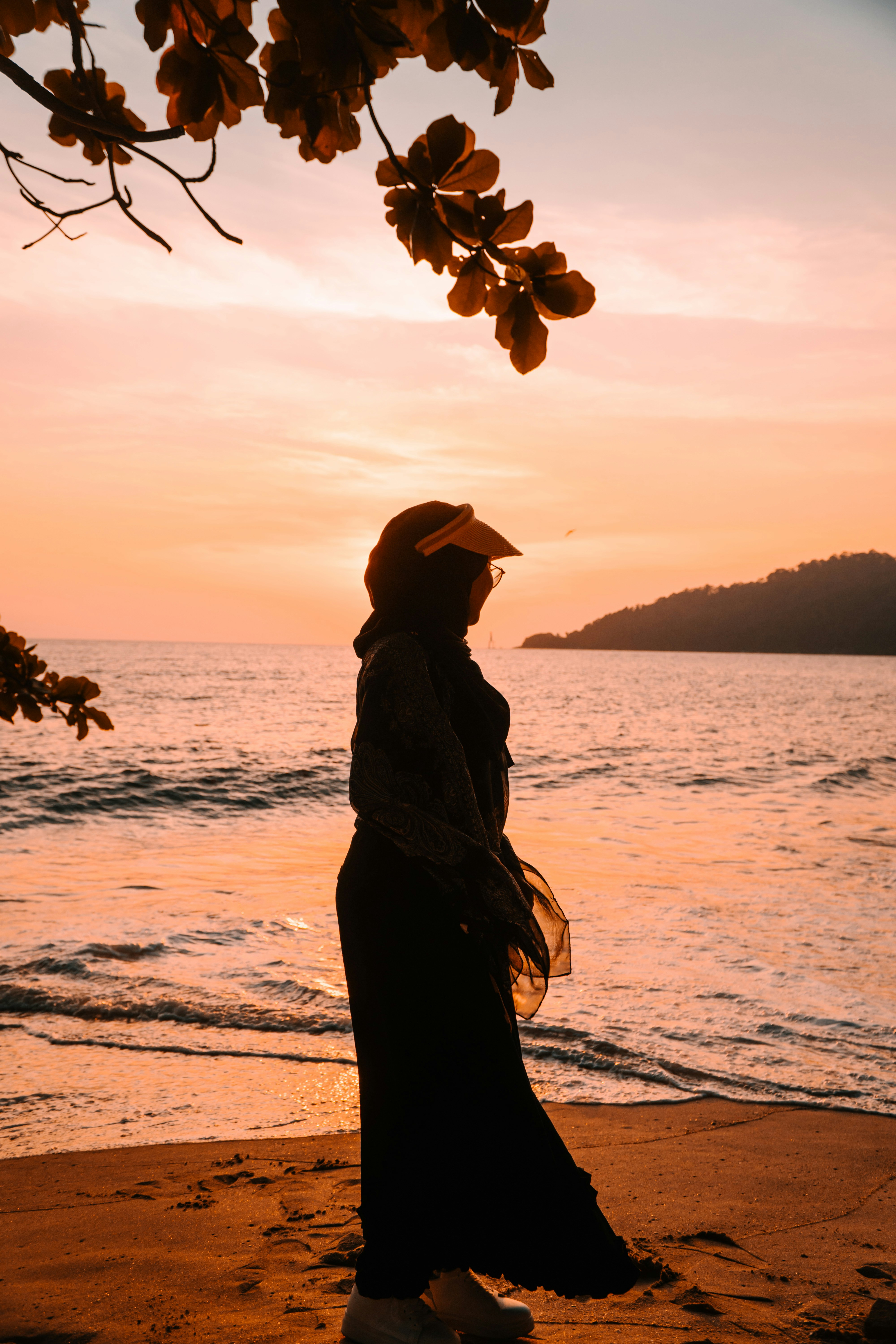 A person in silhouette wearing a headscarf and visor on a beach at low sun