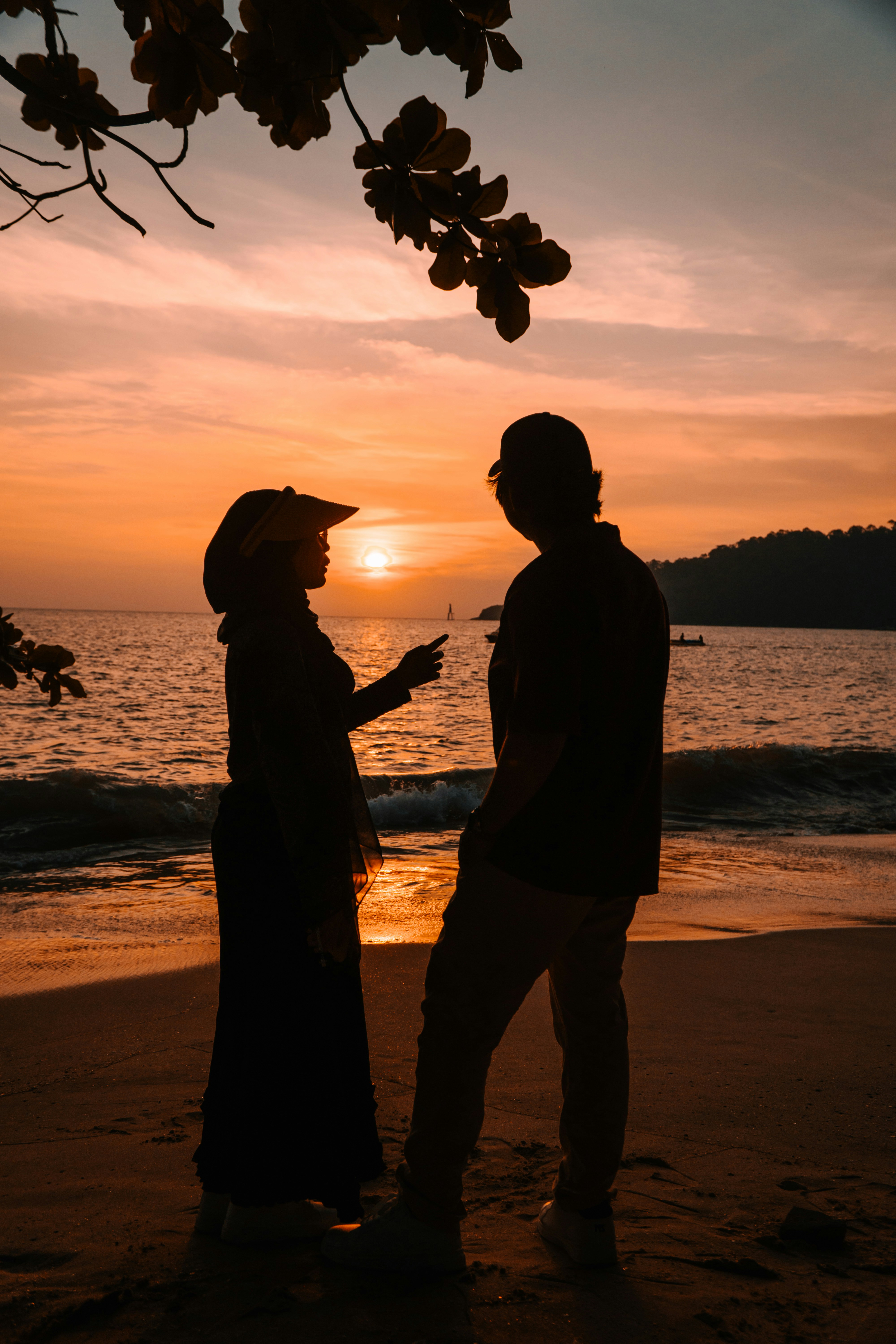 Two people in silhouette on a beach under a warm orange sky