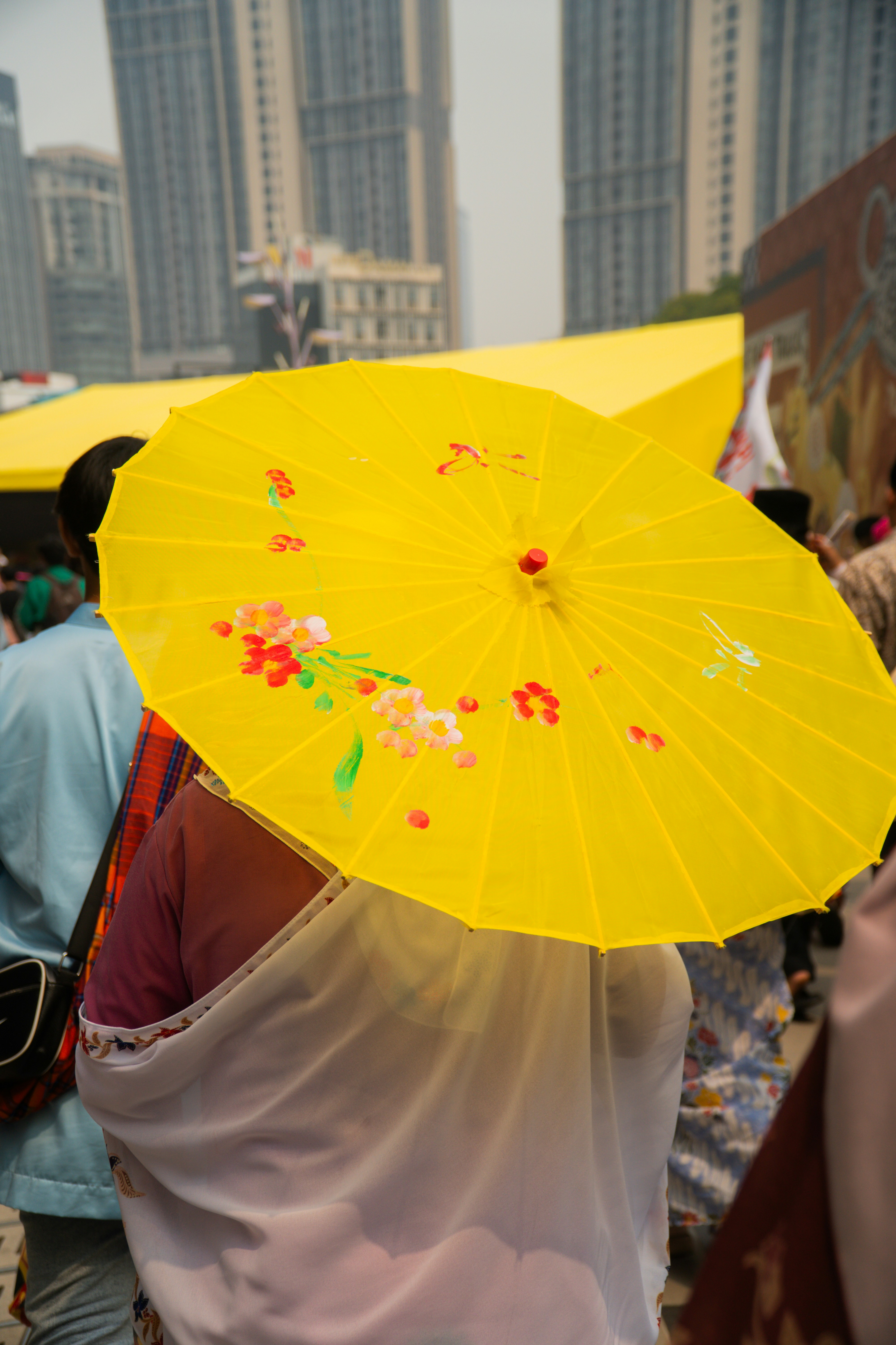 A person holding a bright yellow floral umbrella in a crowded city street