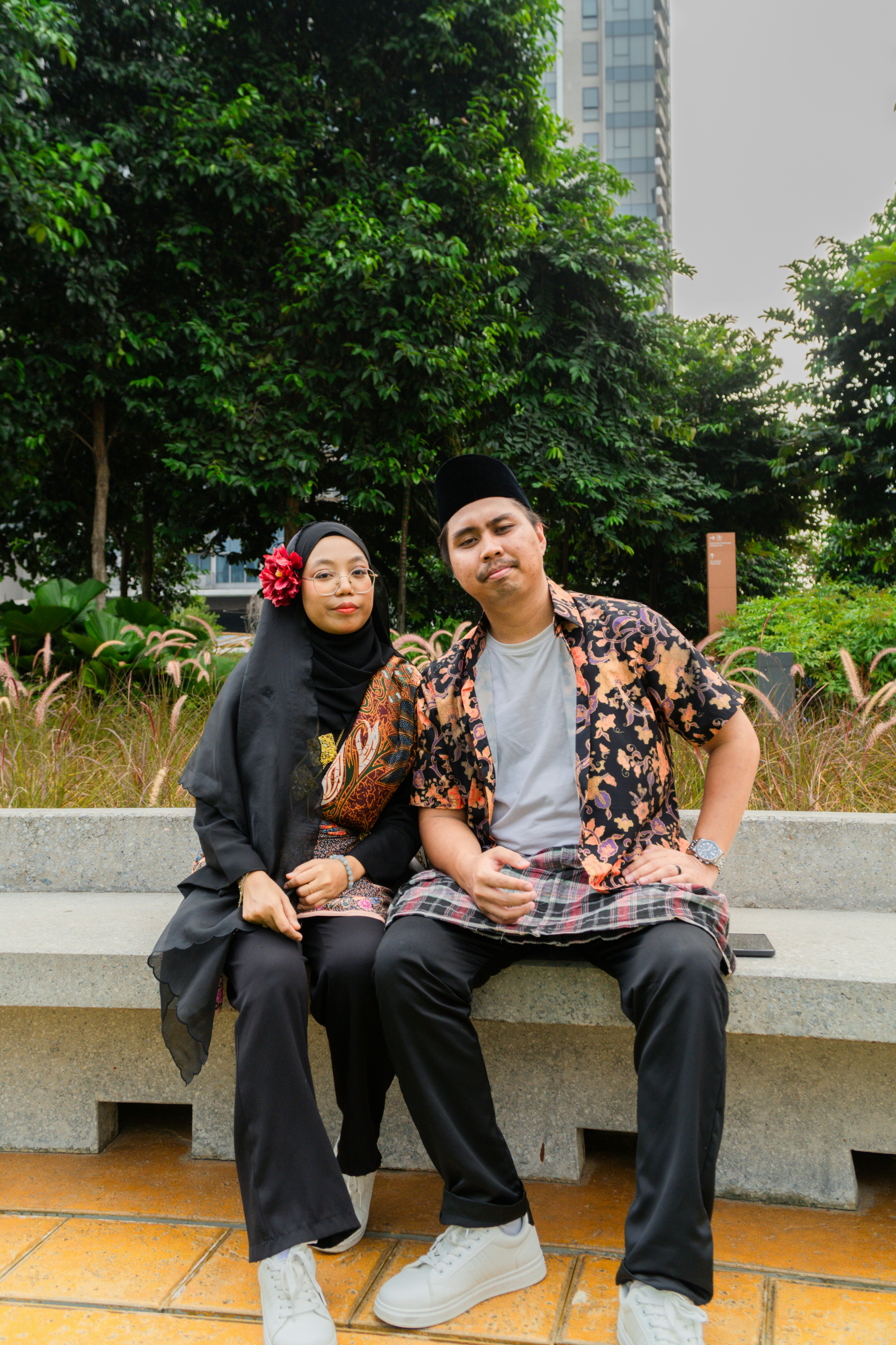A man and a woman in traditional attire sitting on a stone bench outdoors