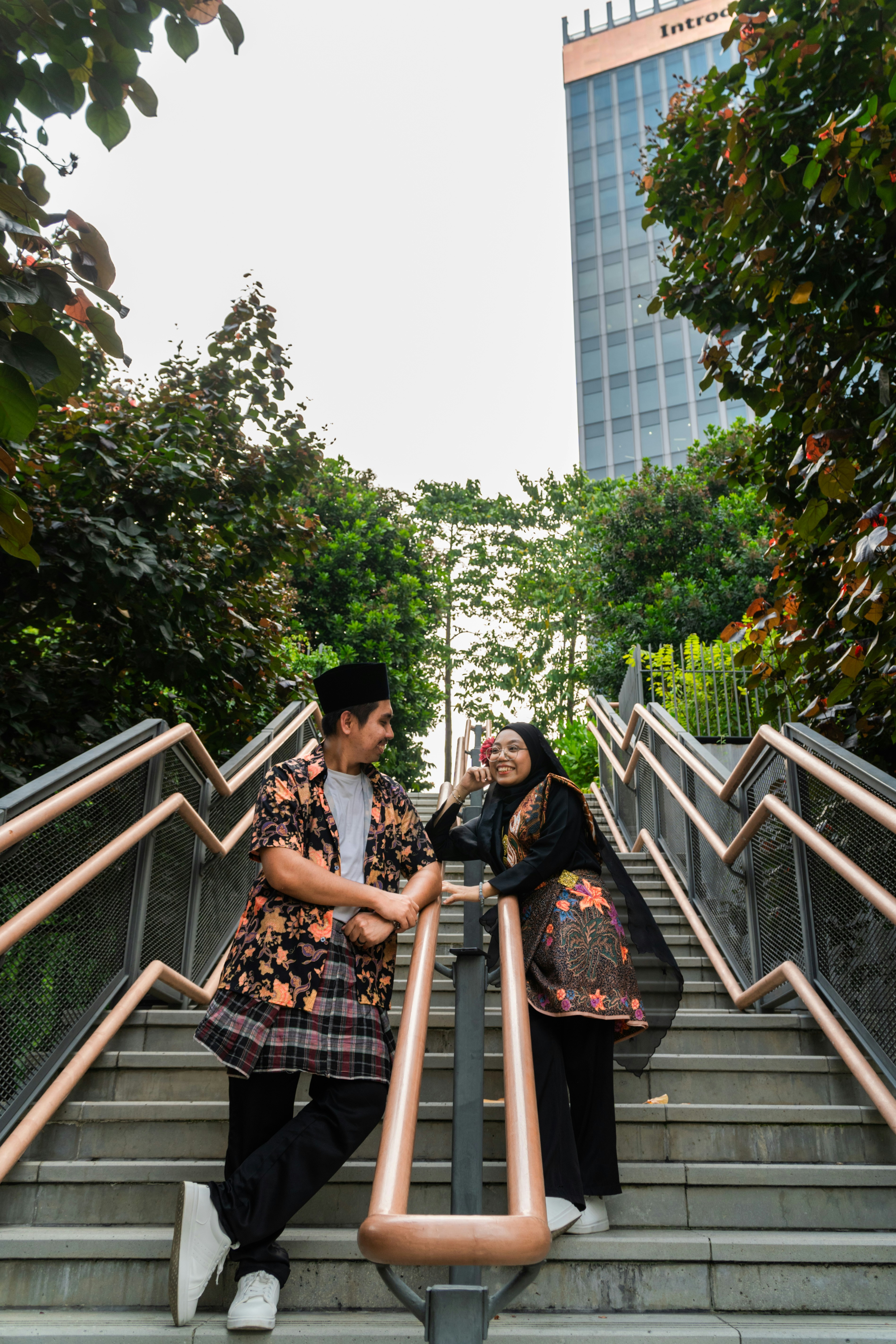 A man and a woman in batik clothing on outdoor stairs near a skyscraper
