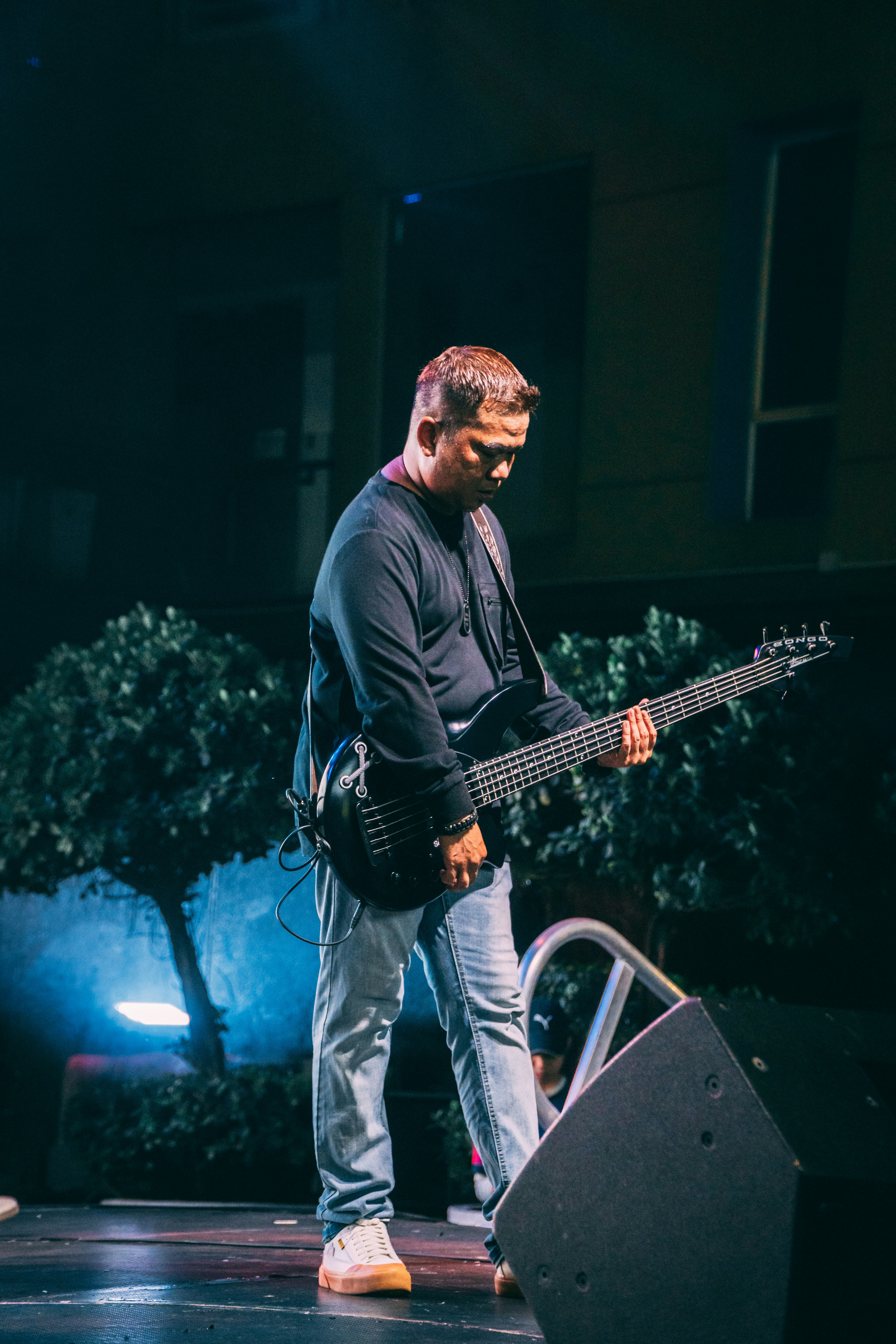 A man playing a black bass guitar on a stage at night