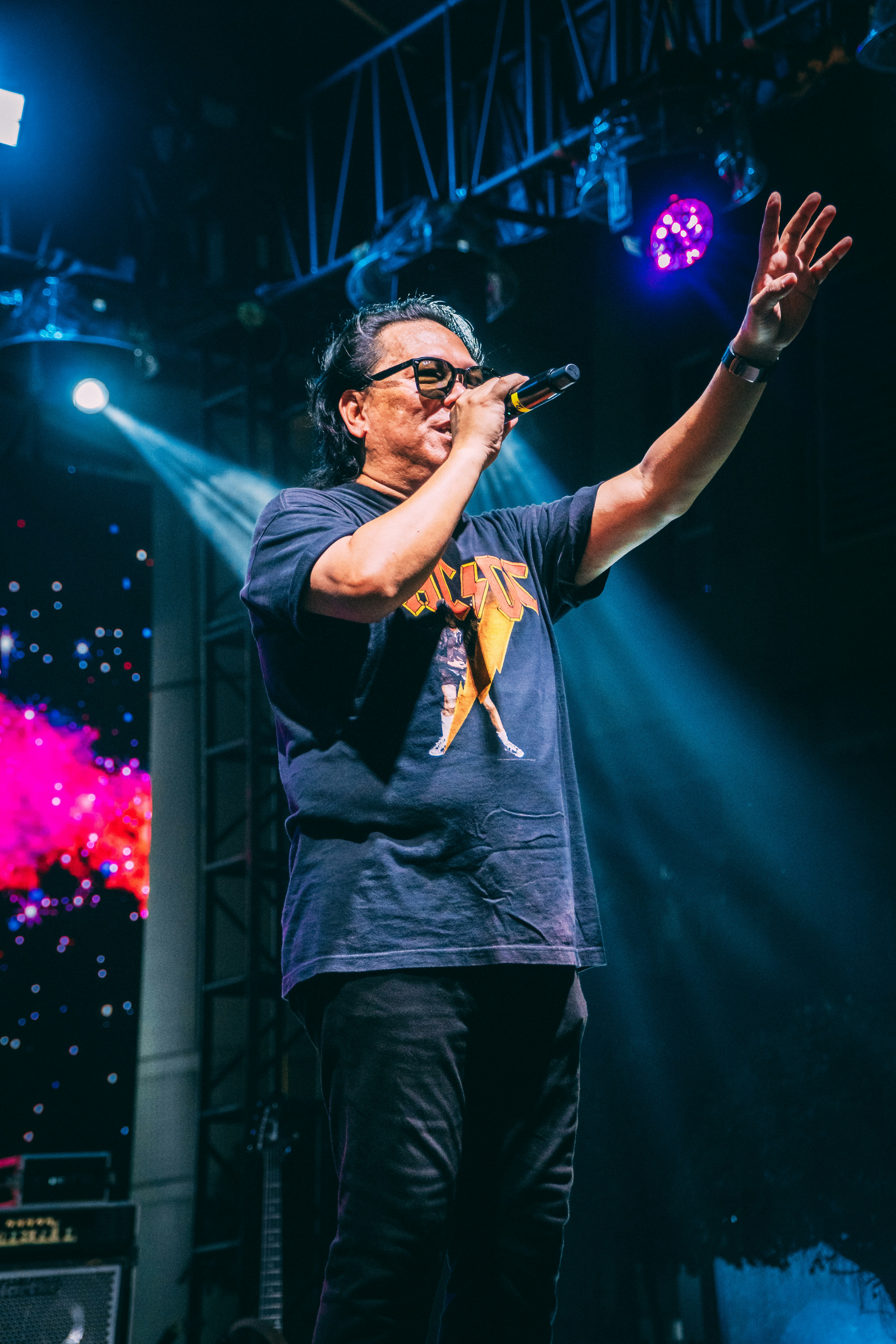 A man in a black t-shirt singing into a microphone on a stage