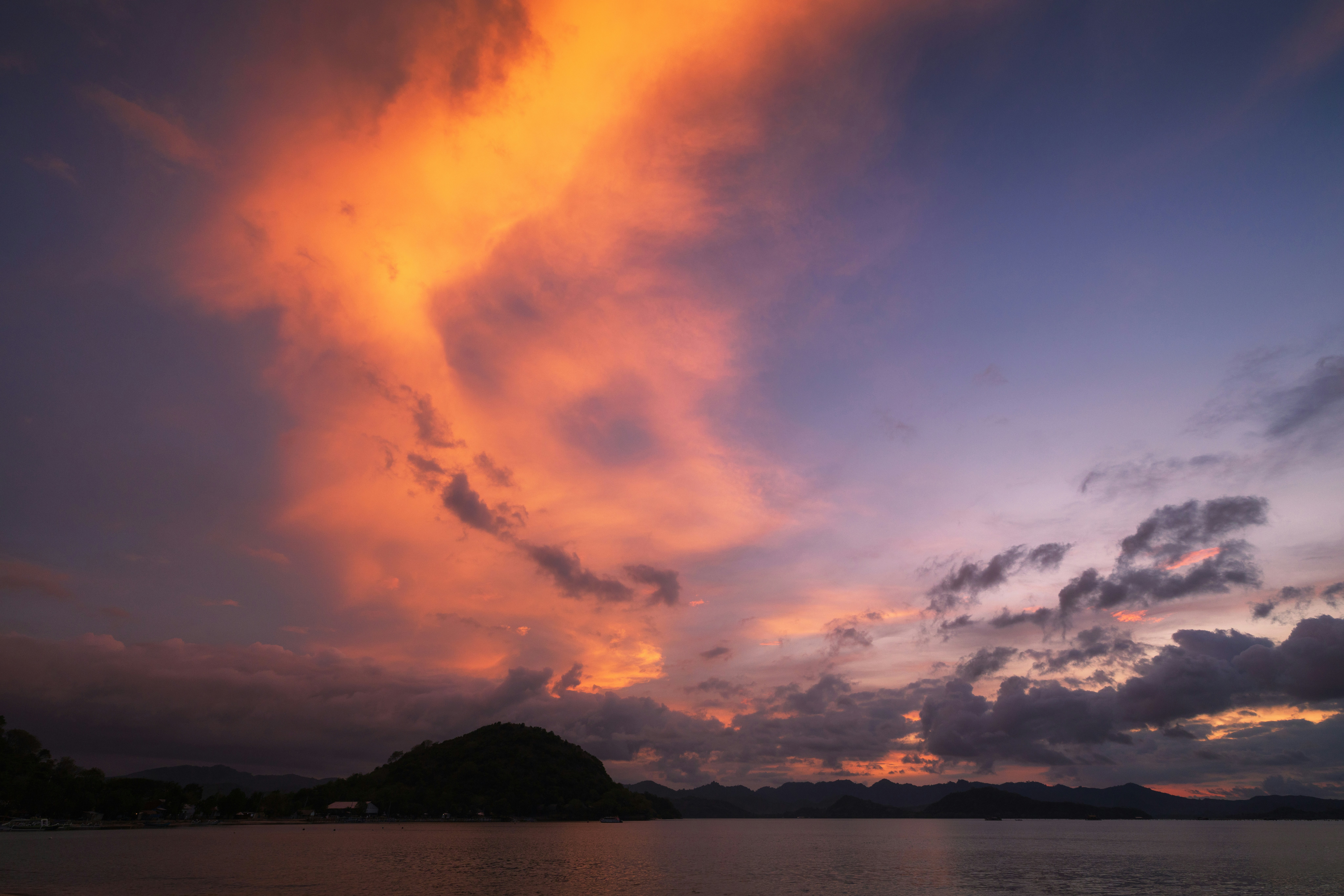 Clouds glowing orange and purple above a dark silhouette of hills and water