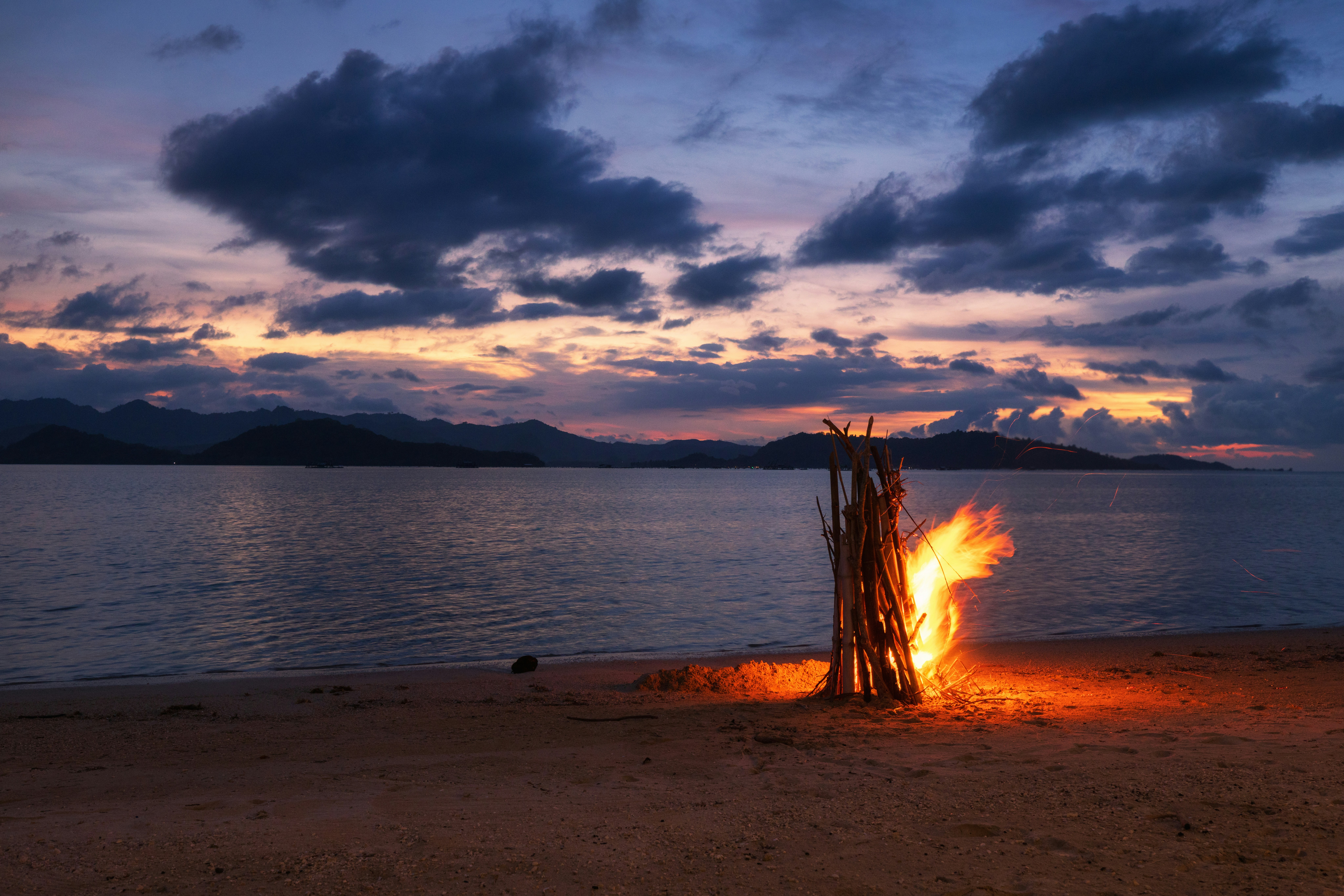 A bright bonfire burning on a sandy beach under a dark cloudy sky