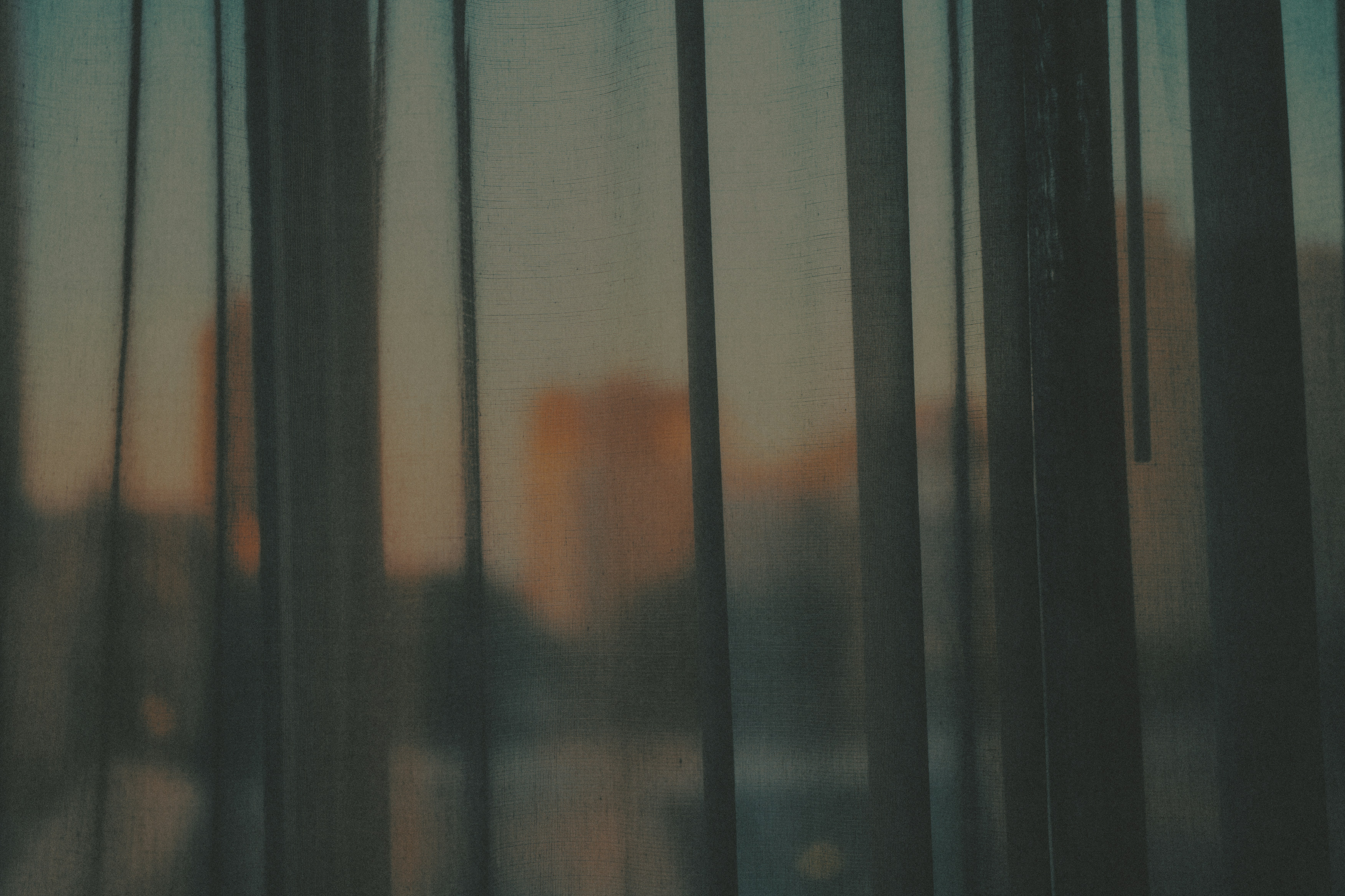 A city skyline visible through thin vertical fabric curtains in warm light