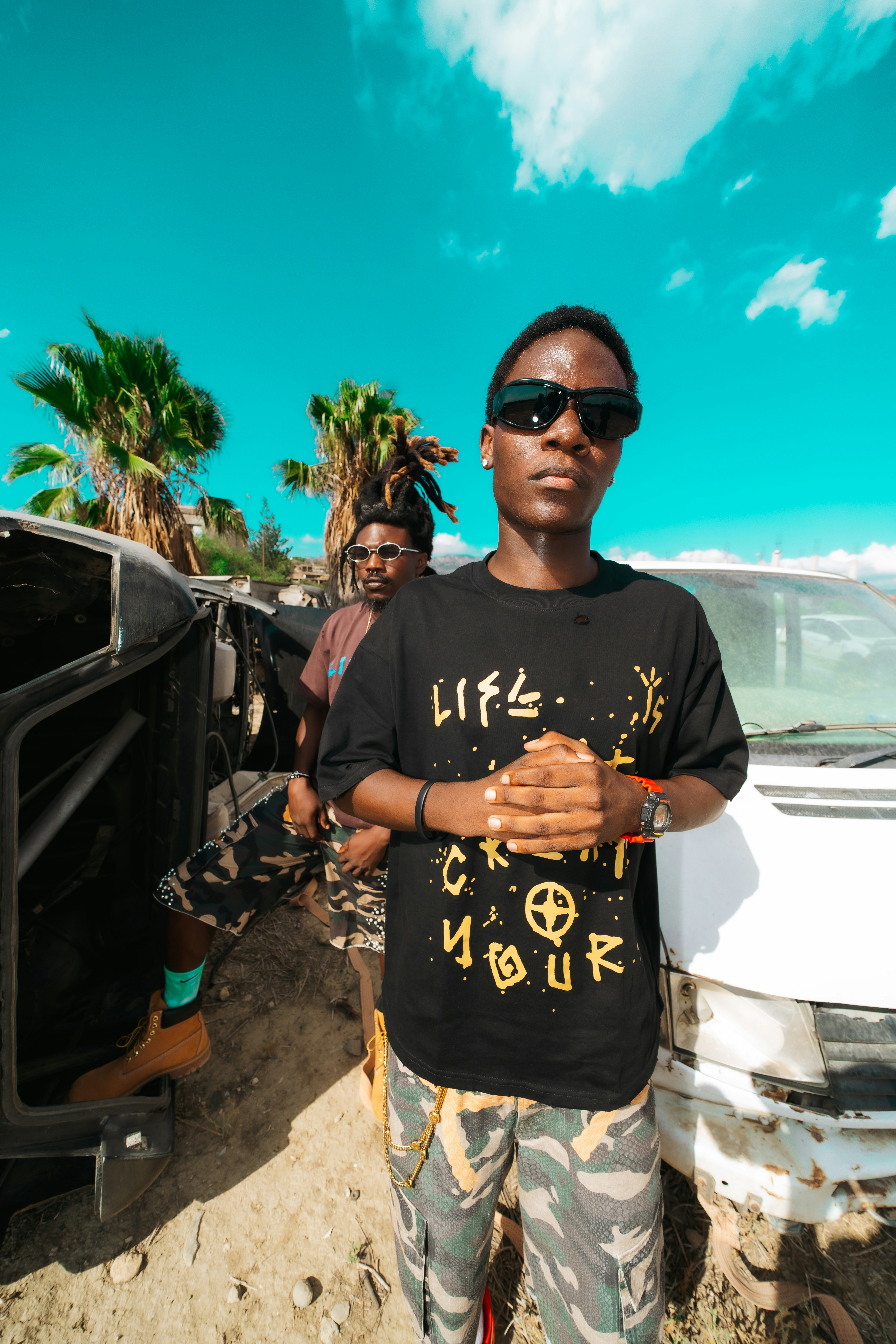 Two men in camouflage shorts and black t-shirts standing near a white van
