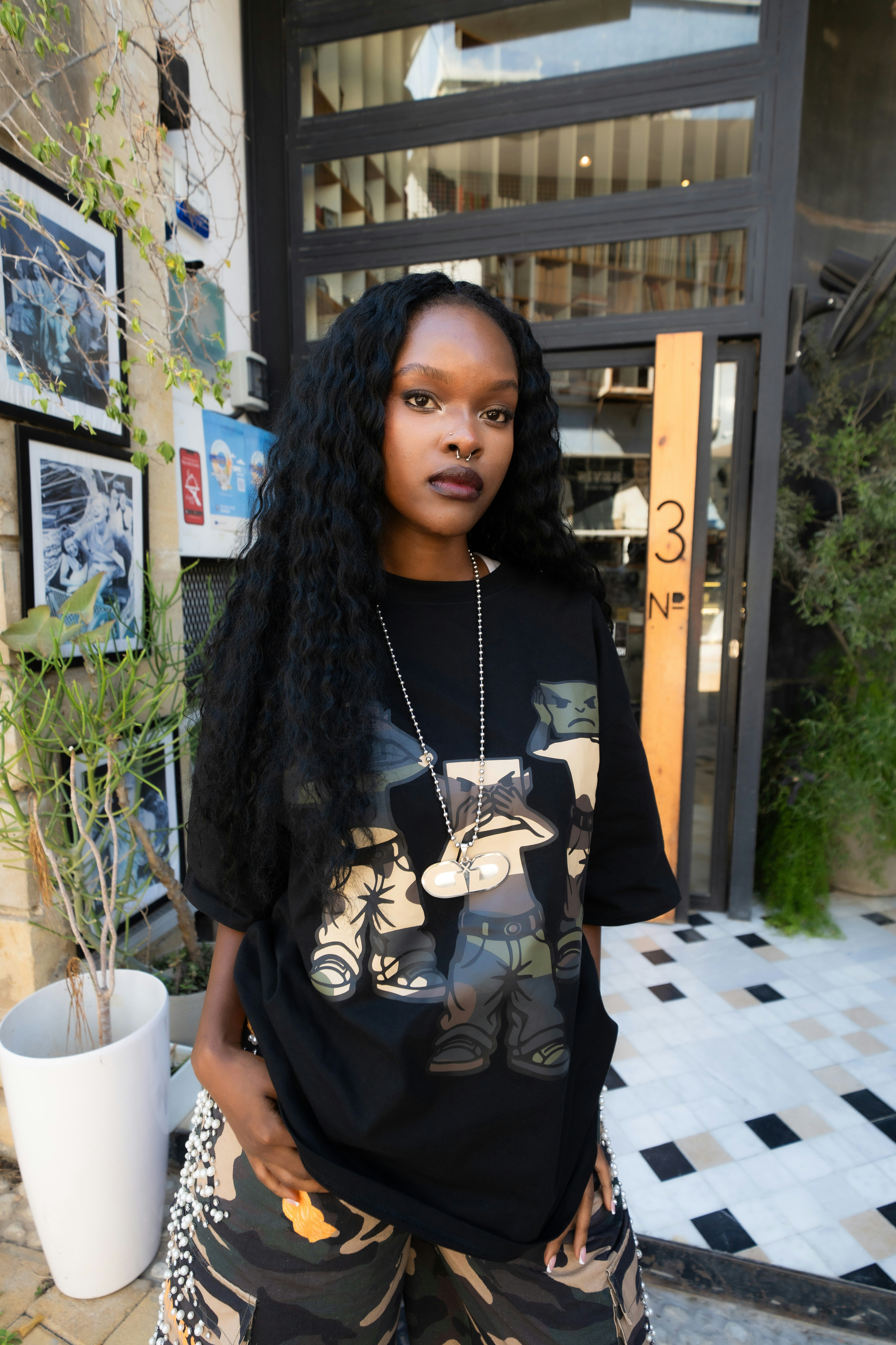 A woman with long dark hair wearing a black graphic t-shirt and camouflage pants
