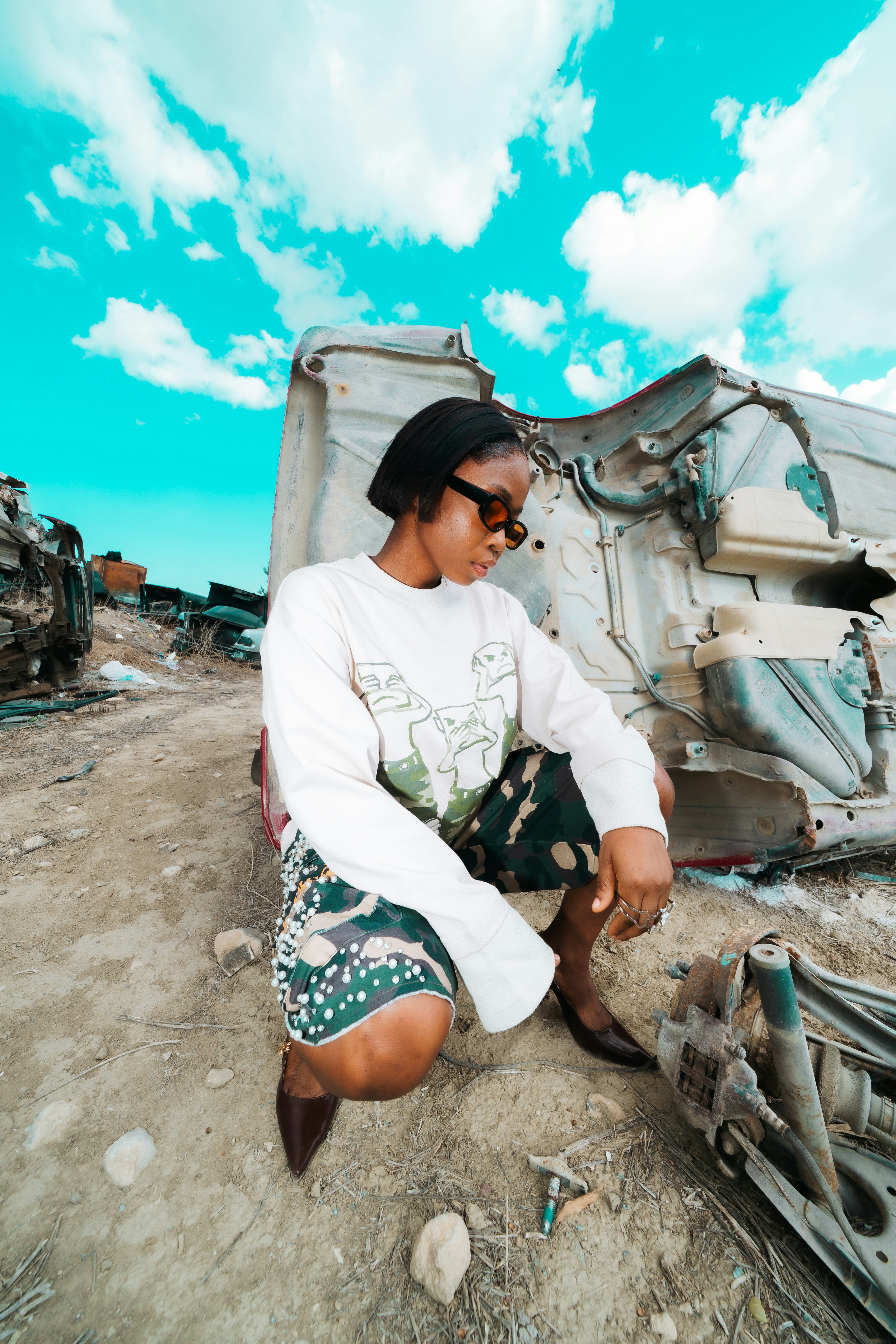 A person in a white sweatshirt and camo shorts crouching by a car chassis