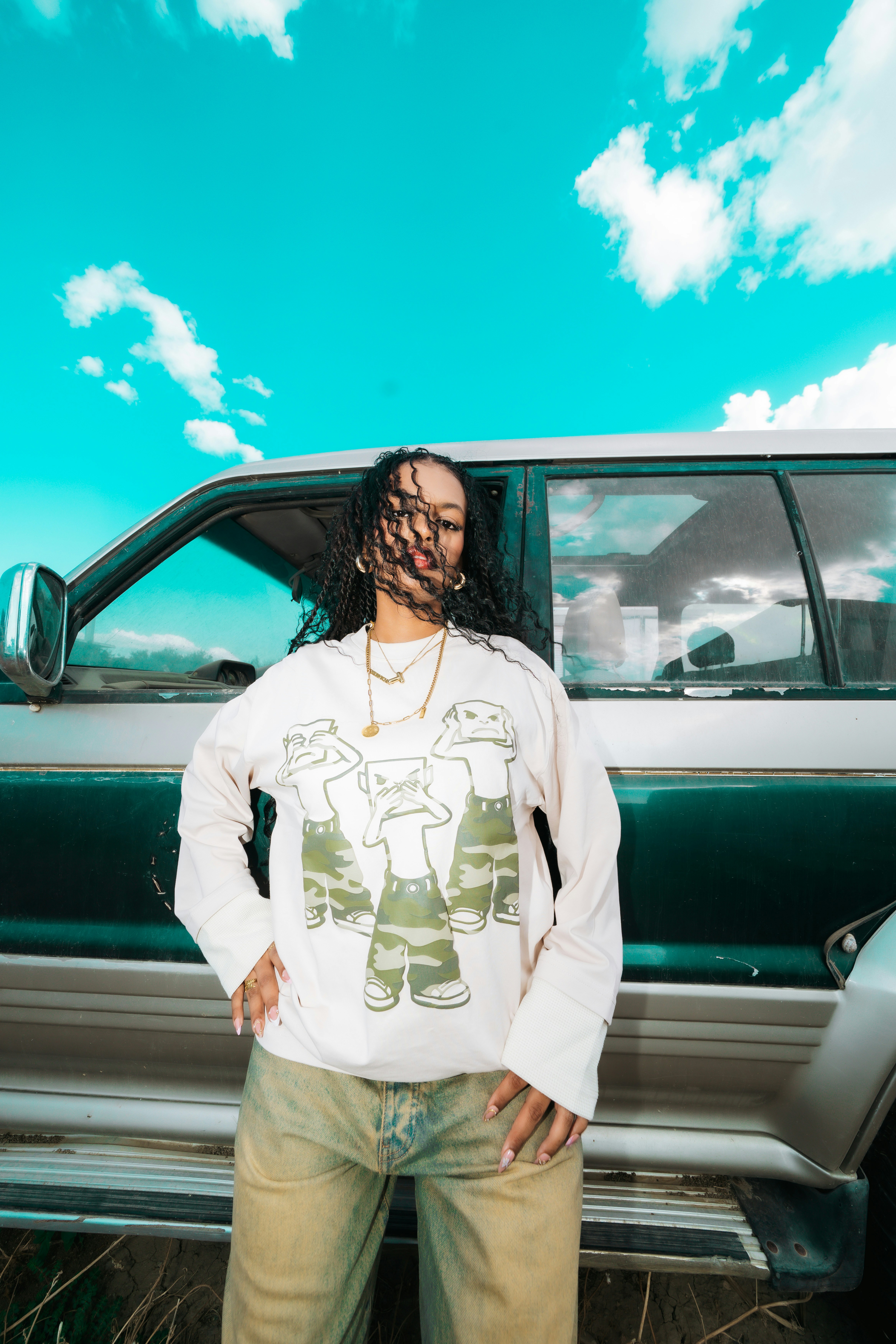 A woman with curly hair in a graphic sweatshirt standing before a green SUV
