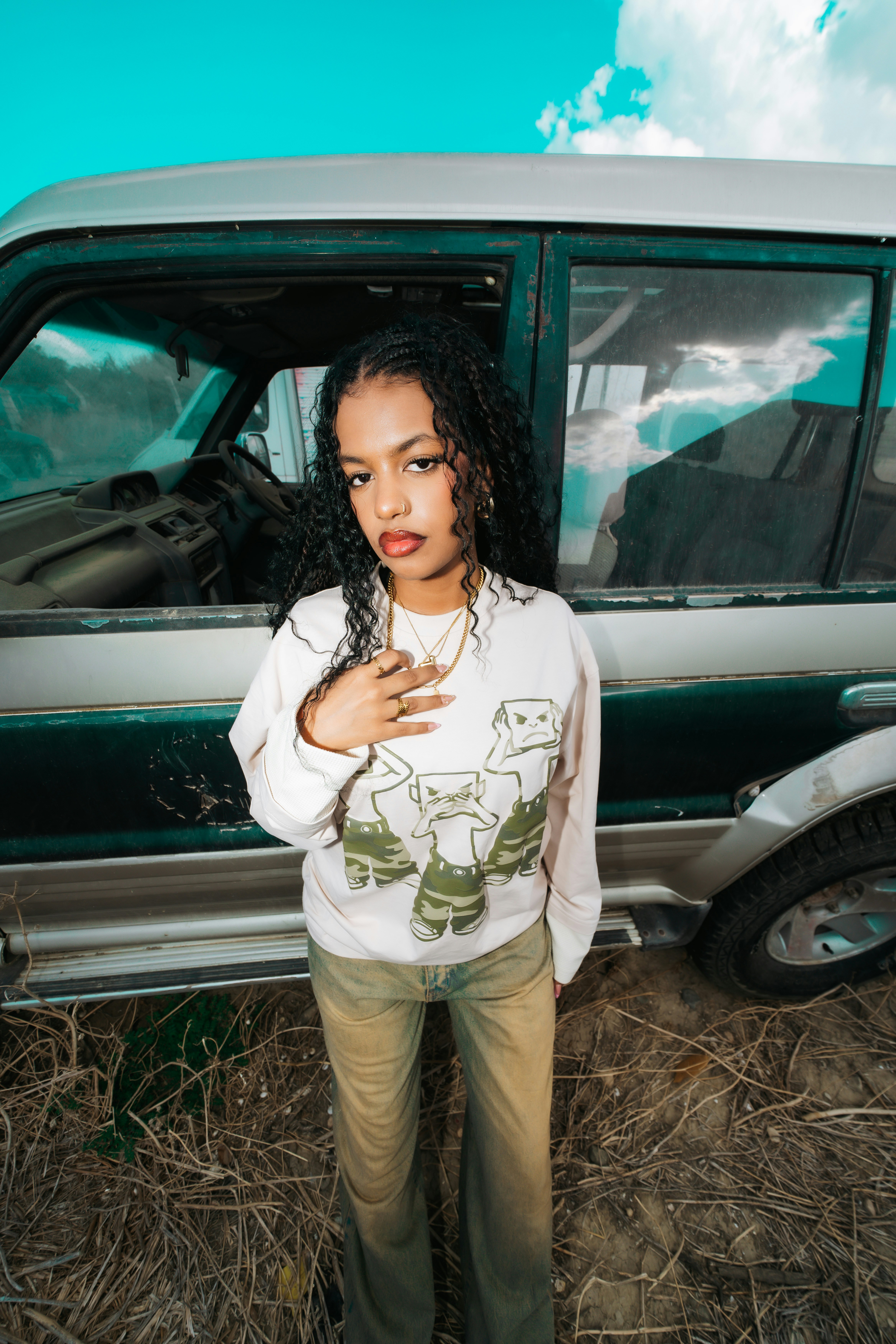 A woman with long curly hair wearing a graphic sweatshirt standing before an SUV