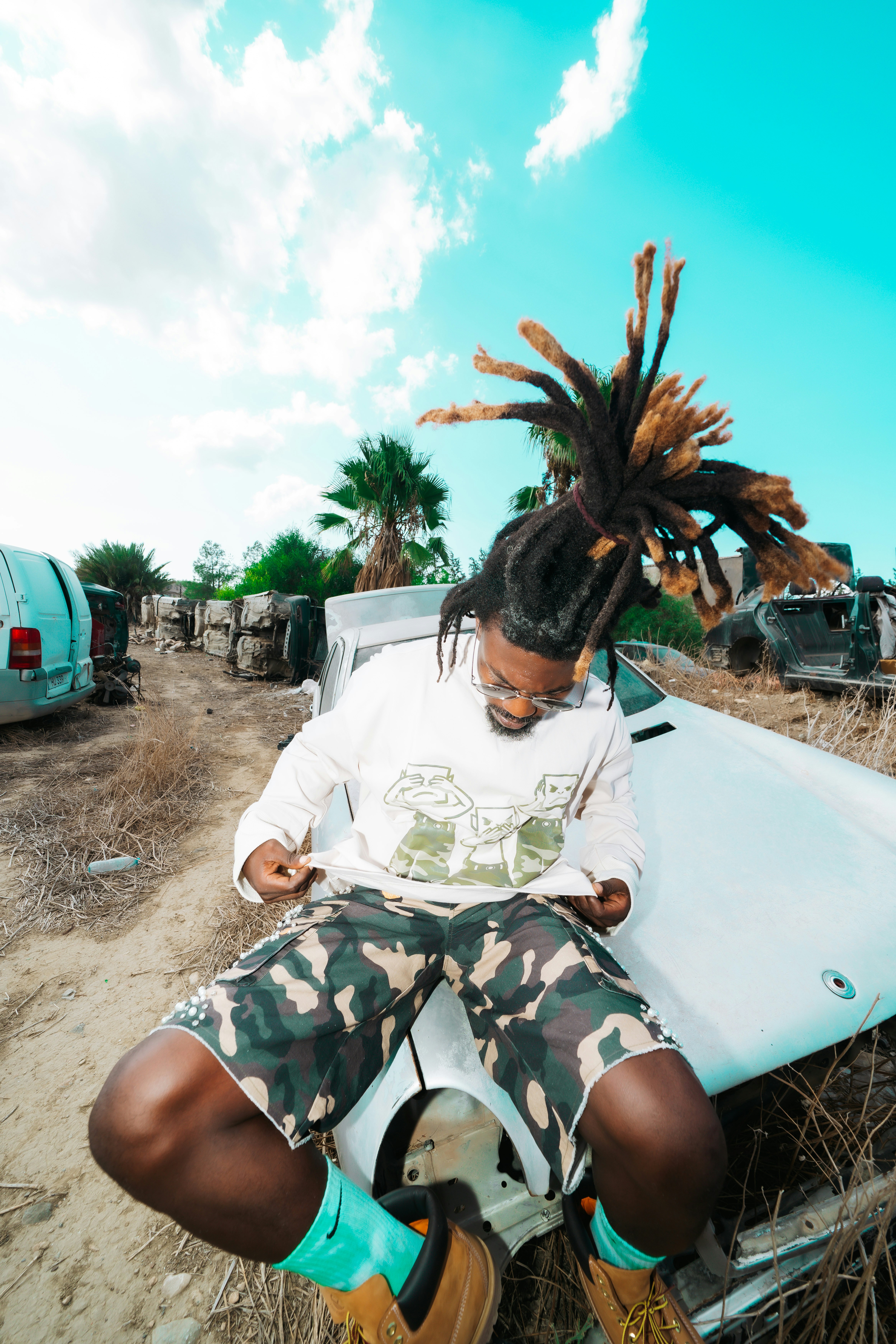 A person with dreadlocks sitting on a wrecked car in a field