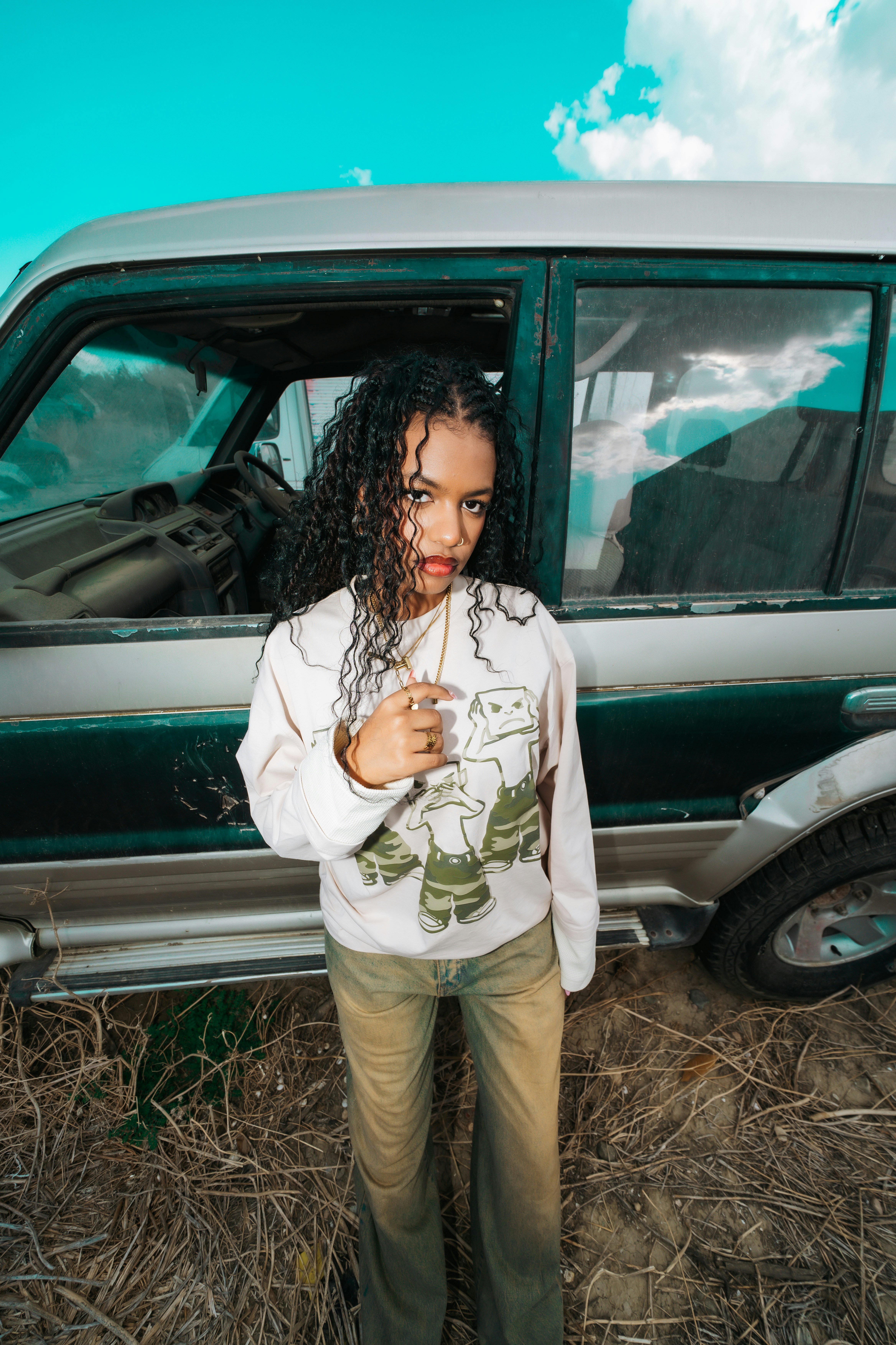 A woman with long curly hair wearing a graphic sweatshirt standing by an SUV