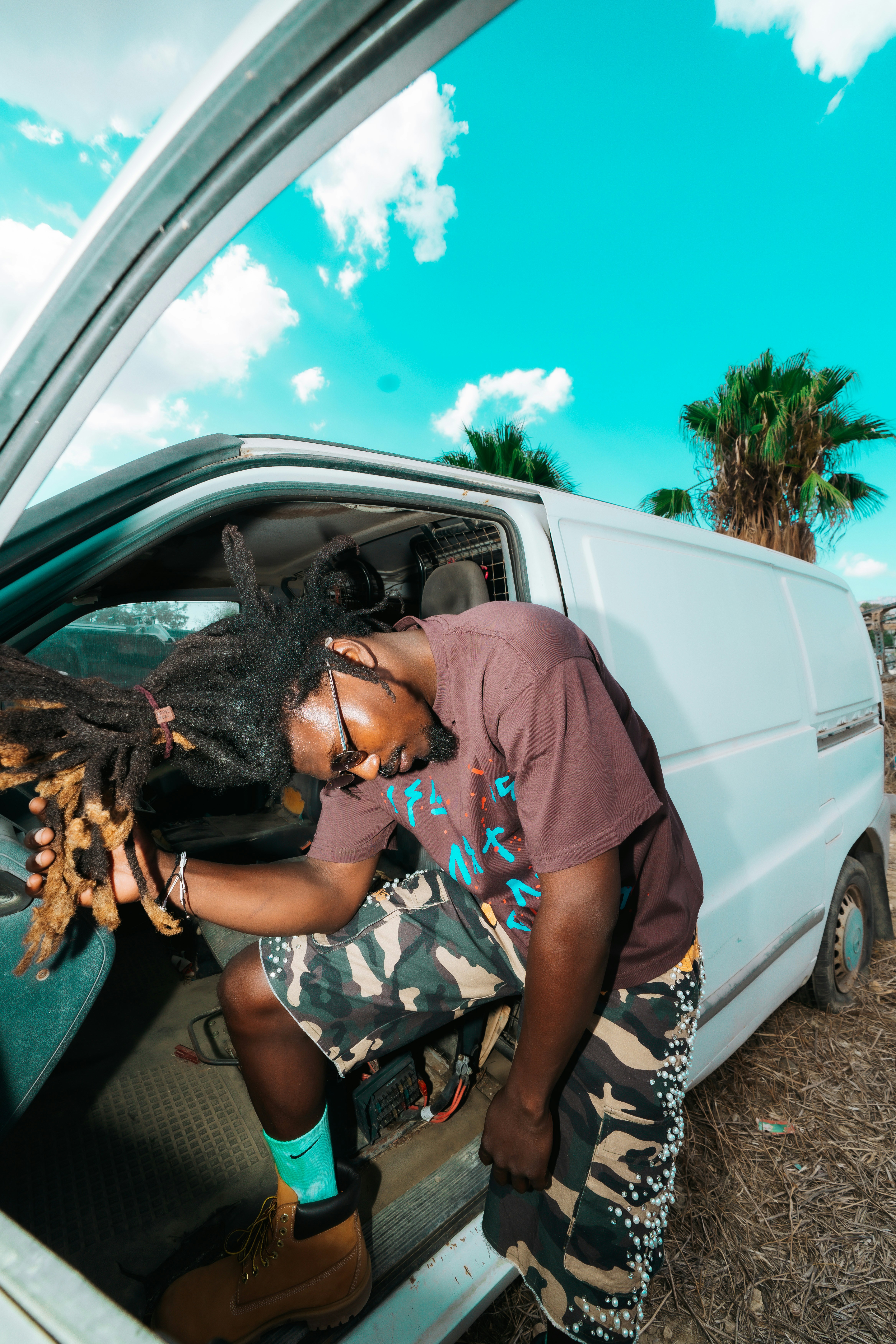A person with dreadlocks leaning out of a white van in a field
