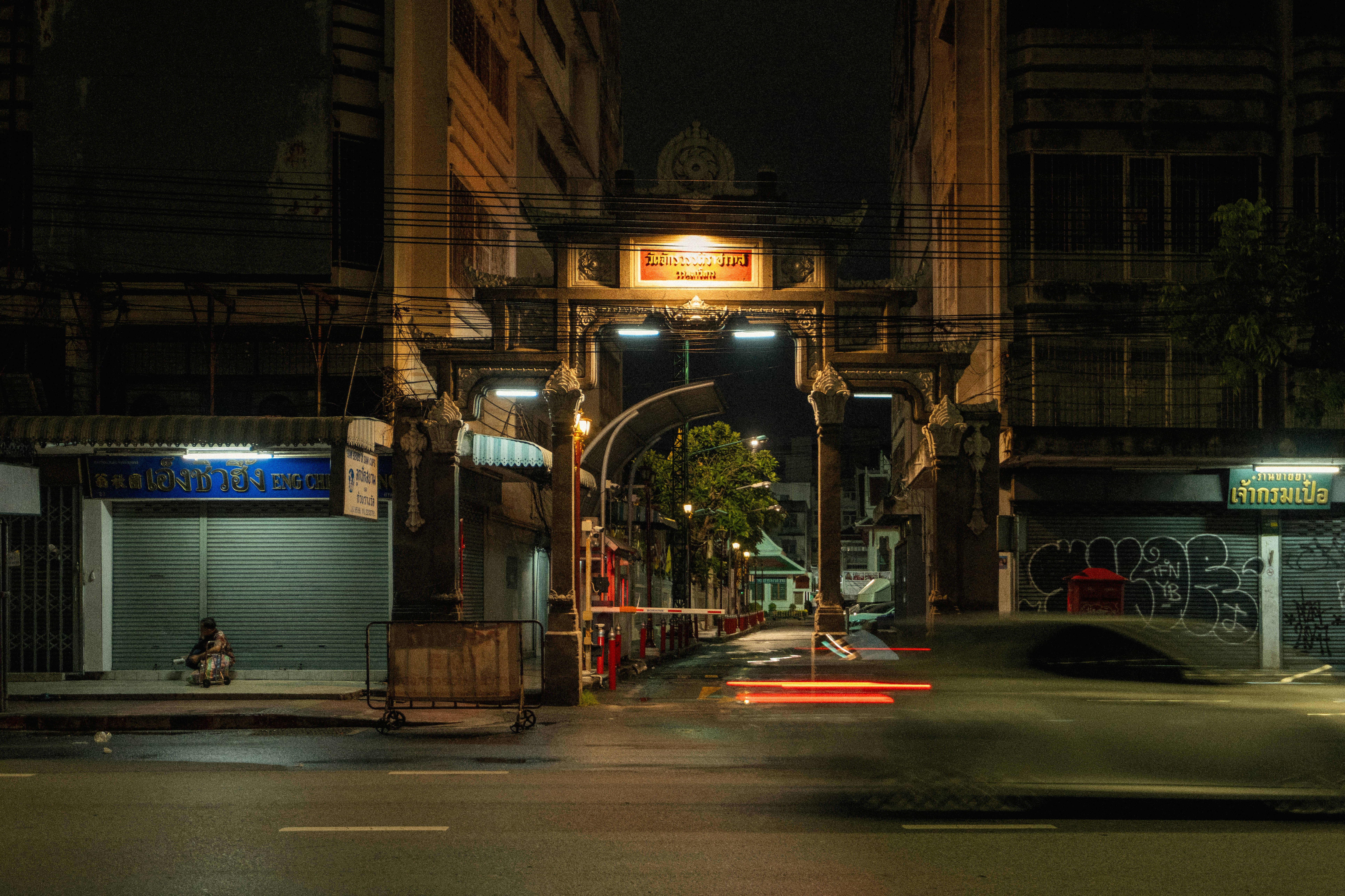 A stone gate at night with a blurred car passing in the foreground