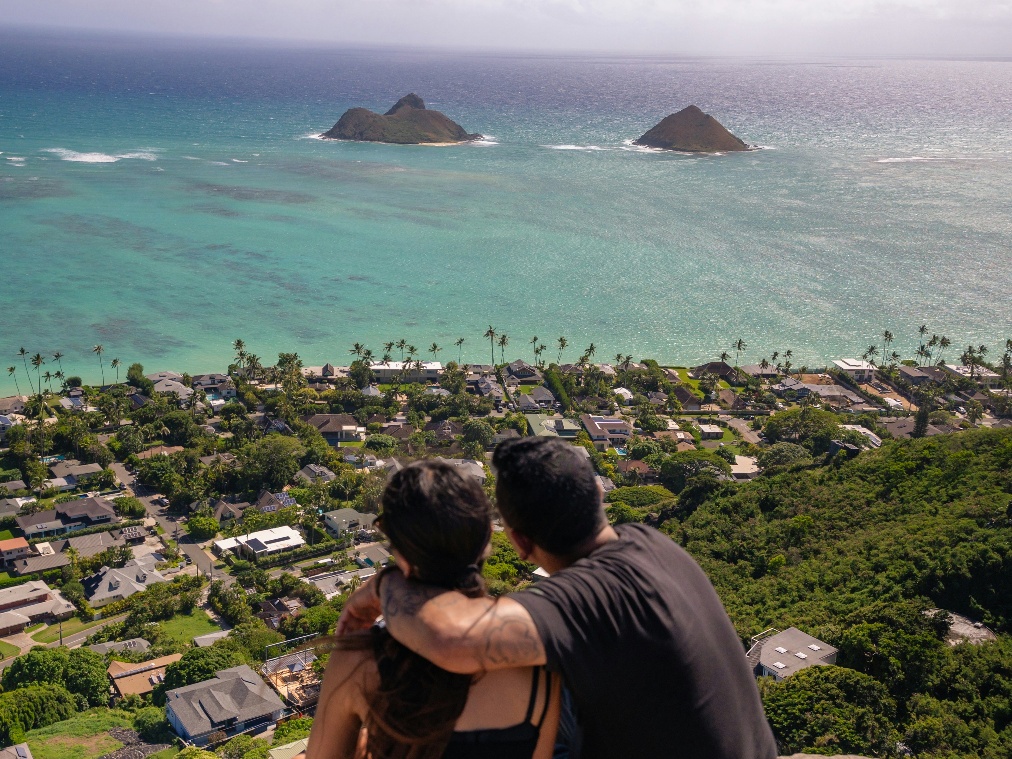 A couple looking out over a coastal town and turquoise ocean with two islands