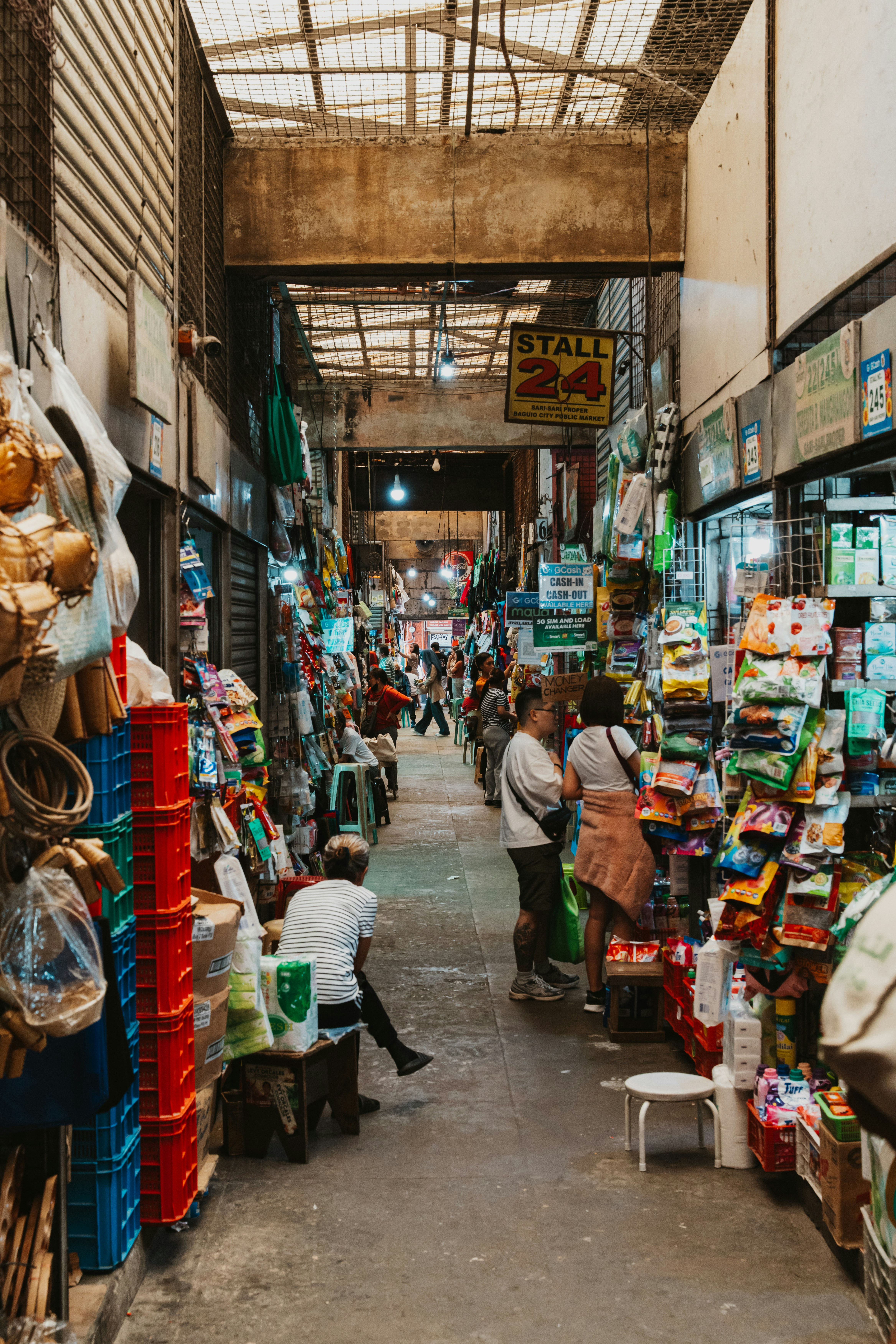 People browsing narrow aisles in a crowded public market with hanging goods